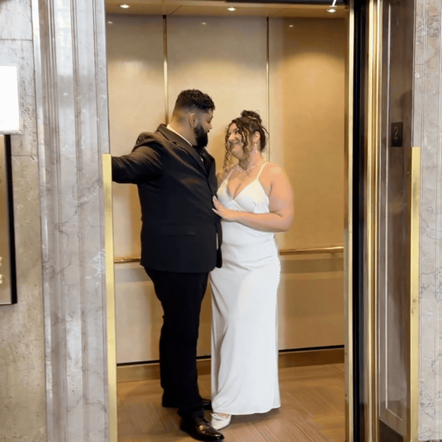 A couple in an elevator, dressed in formal attire, gazing at each other romanticly.