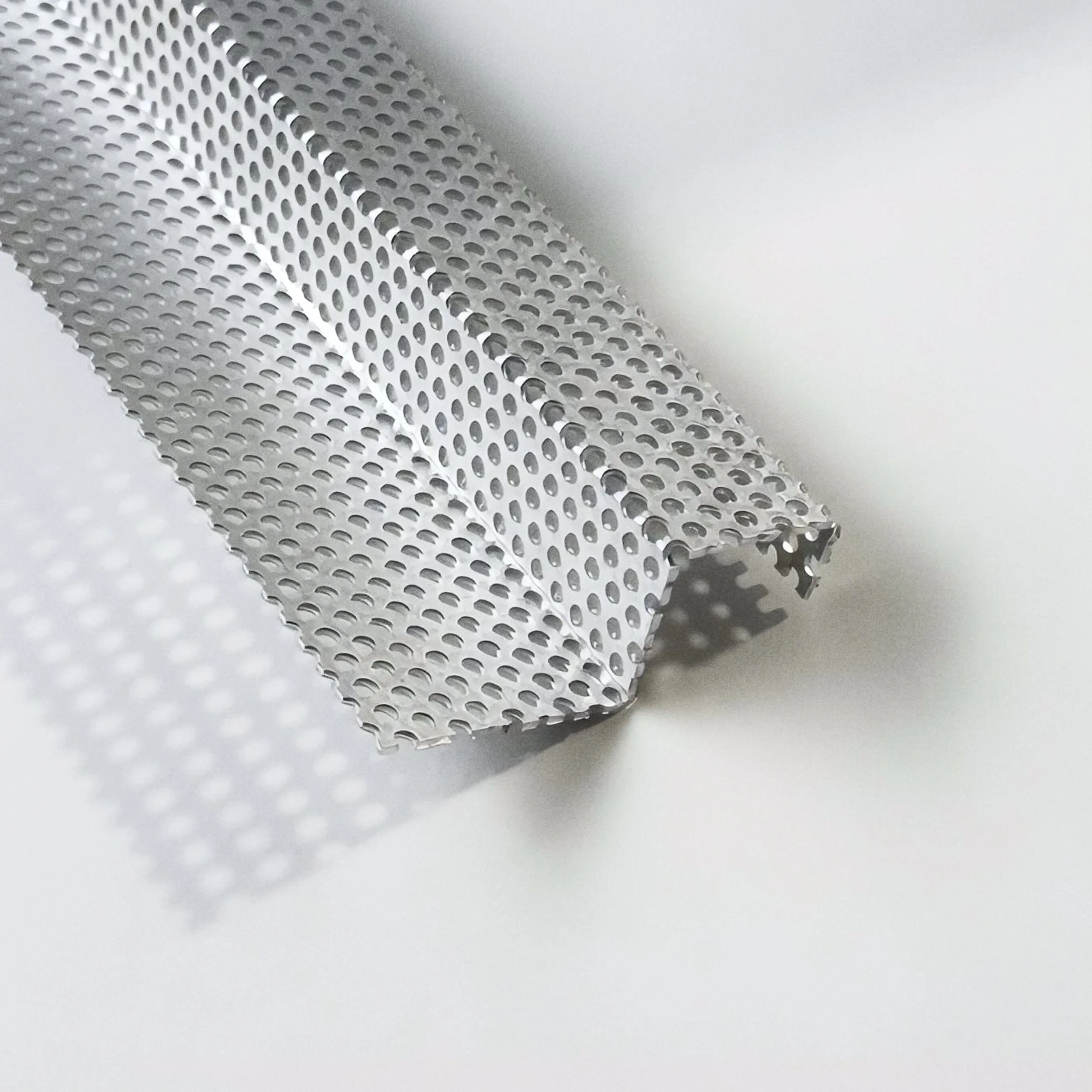 Close-up of a perforated metal sheet with round holes, lying on a white surface.