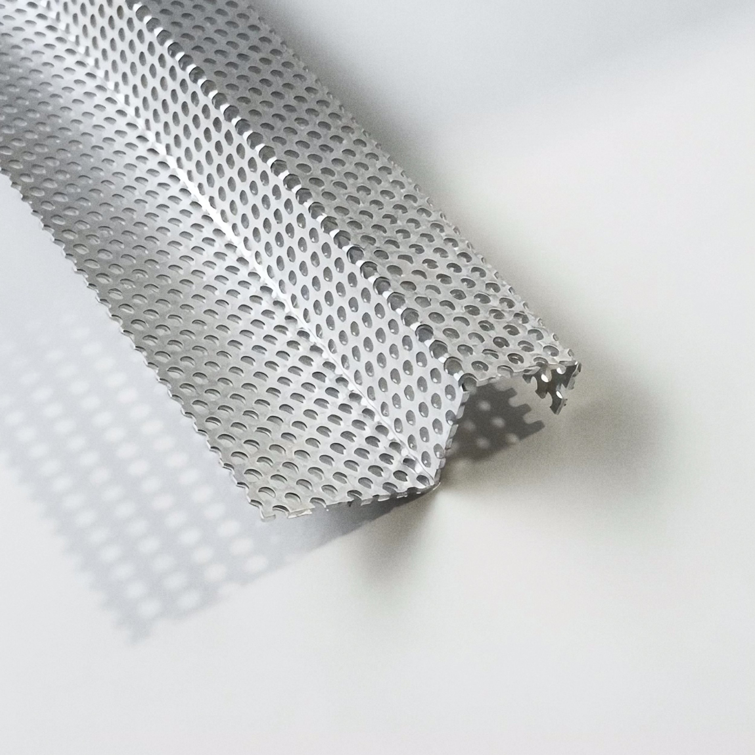 A rolled sheet of perforated metal with evenly spaced circular holes, placed on a white surface.