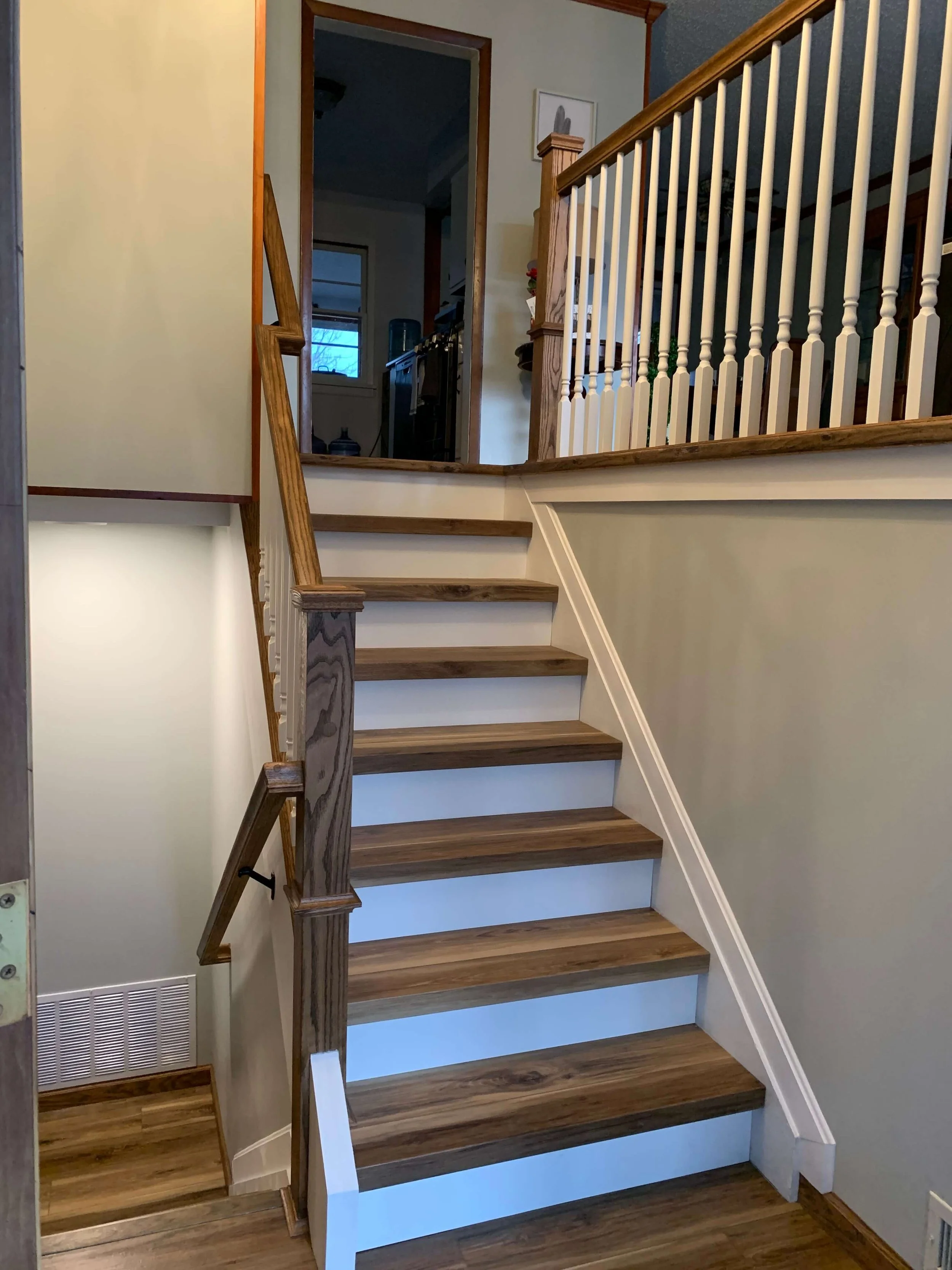 Wooden stairs leading to an upper floor with a wooden railing and white wall paneling.
