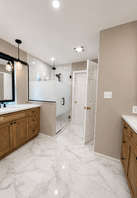 Modern bathroom with wooden vanities, marble floors, a glass shower enclosure, and neutral painted walls.