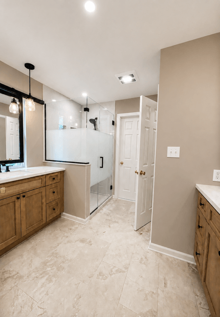 Bathroom with wooden vanities, a glass shower enclosure, a mirror, and beige tile flooring.