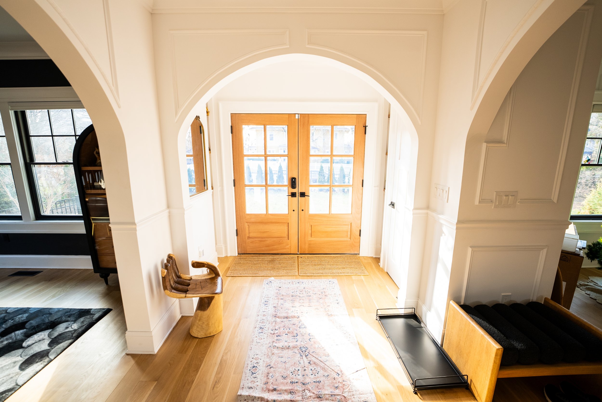 Entryway with wooden double doors, hardwood floor, a small rug, and a wooden bench on the right side.