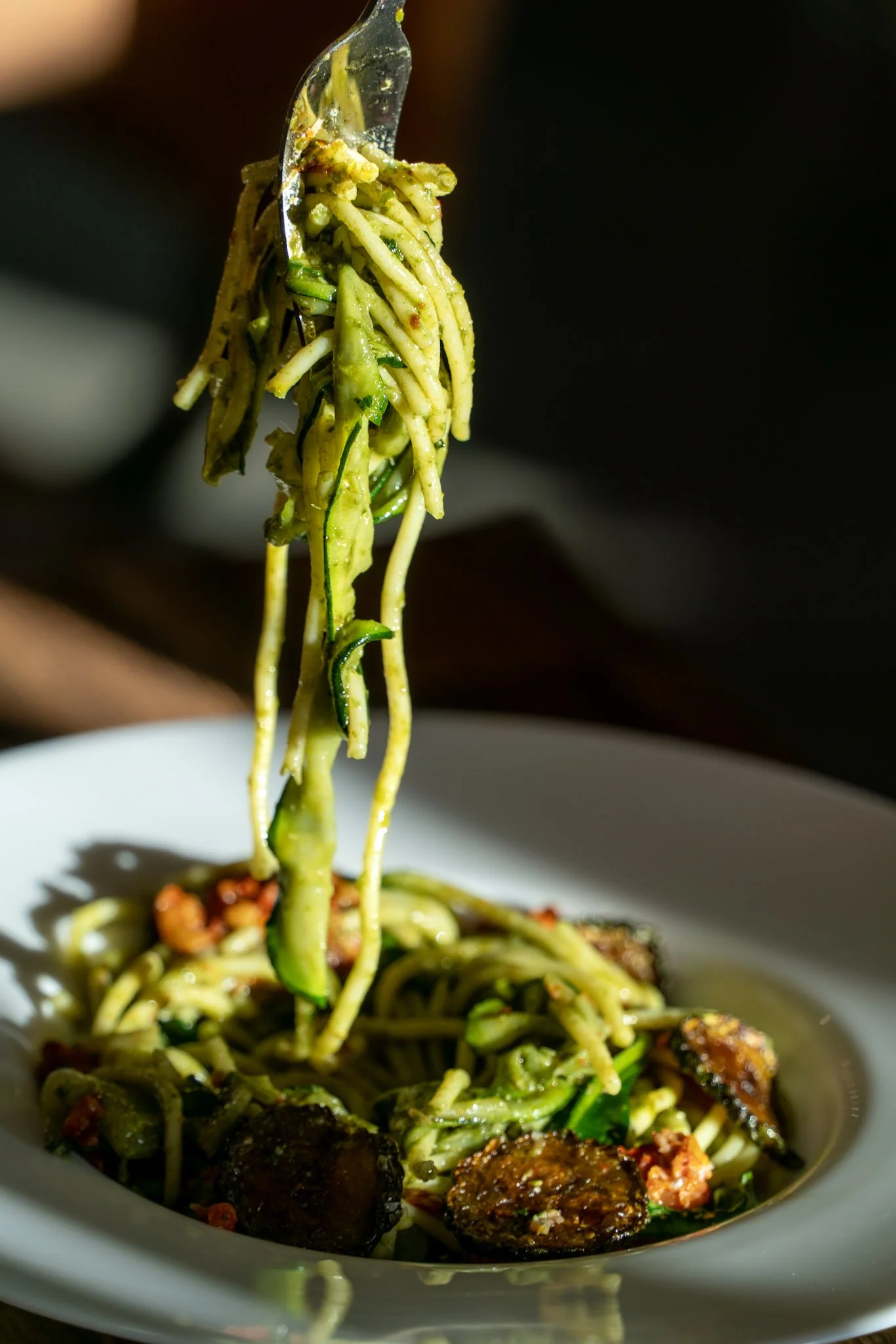 Close-up of a fork lifting a portion of zucchini noodles with roasted vegetables from a white plate.
