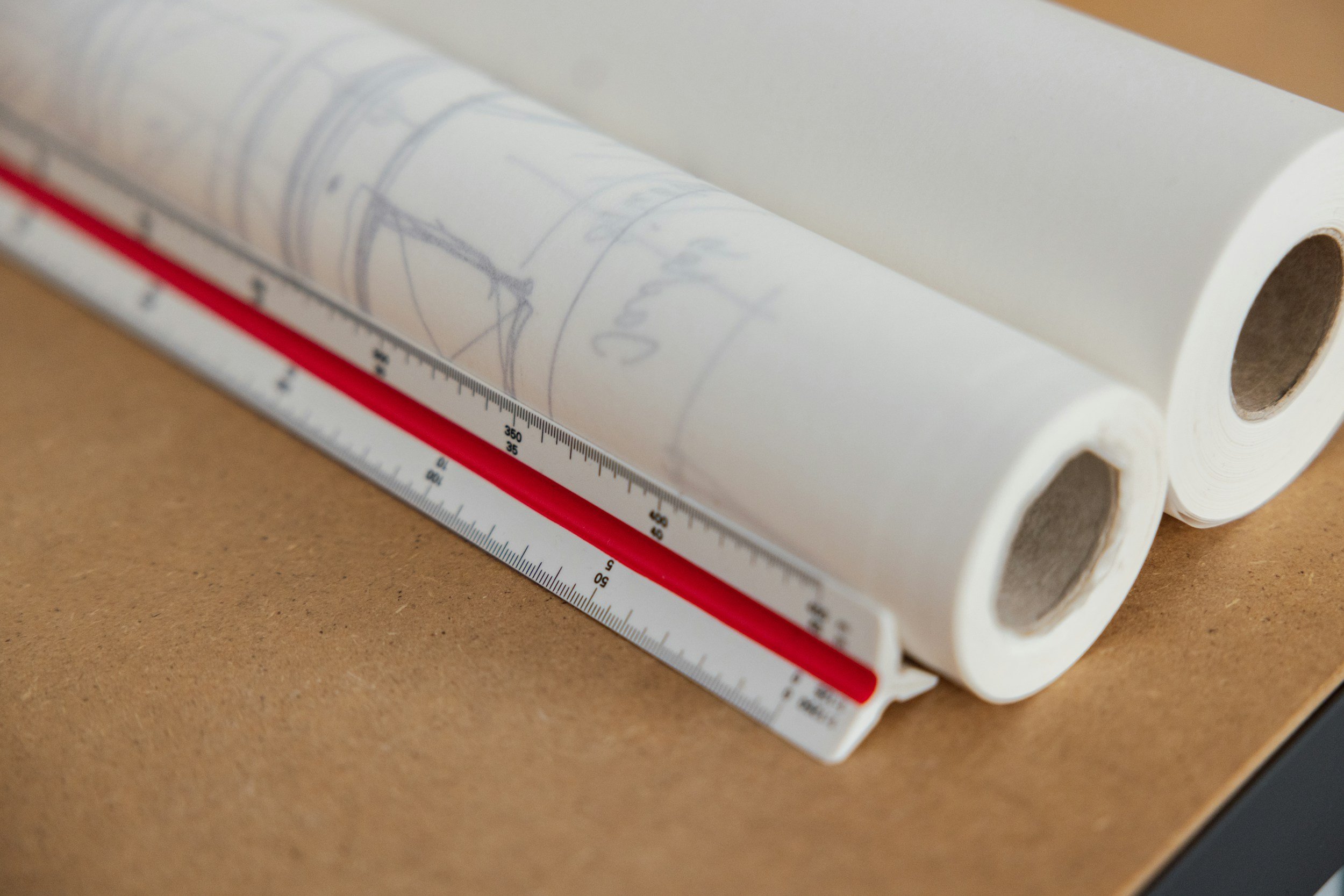 Three rolled-up architectural blueprints and a measuring ruler on a brown surface.