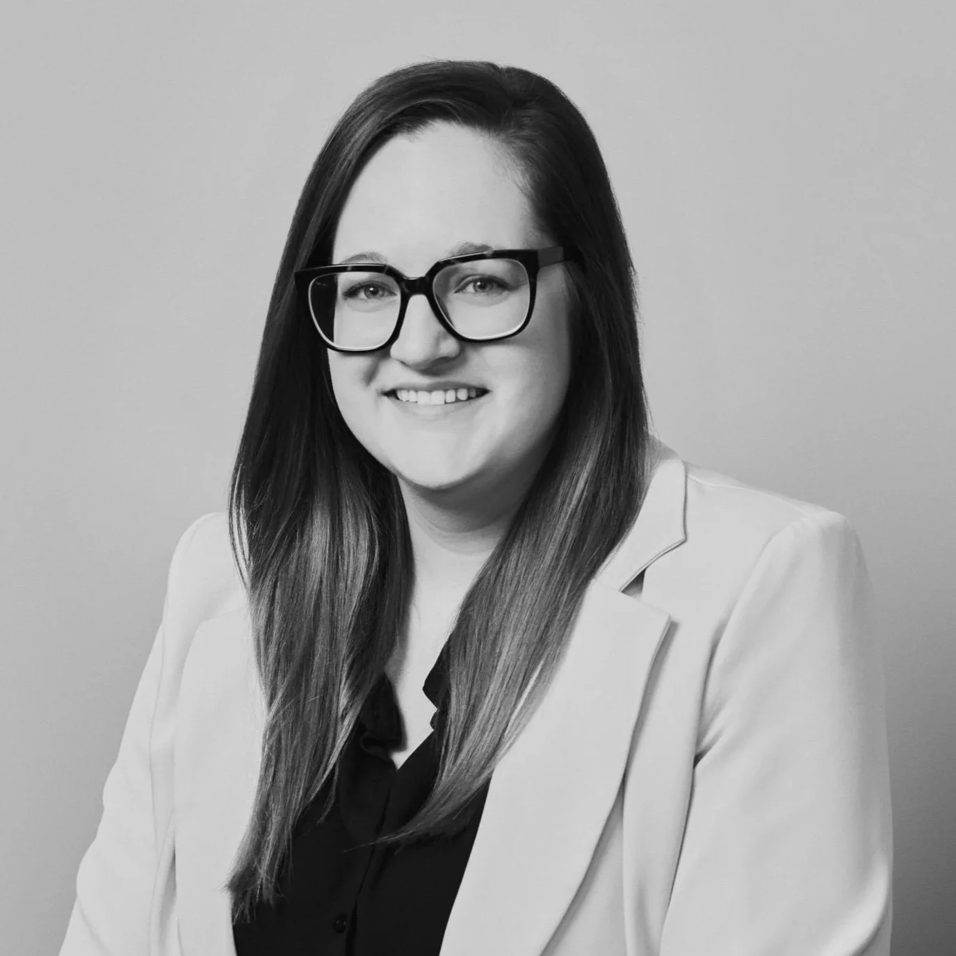 Portrait en noir et blanc d'une femme souriante portant des lunettes et une veste claire.