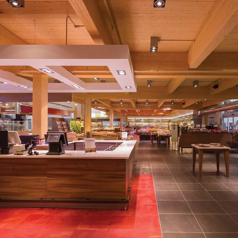 Intérieur d'une superette avec caisses enregistreuses, étals de fruits et légumes, et rayon de produits en arrière-plan.