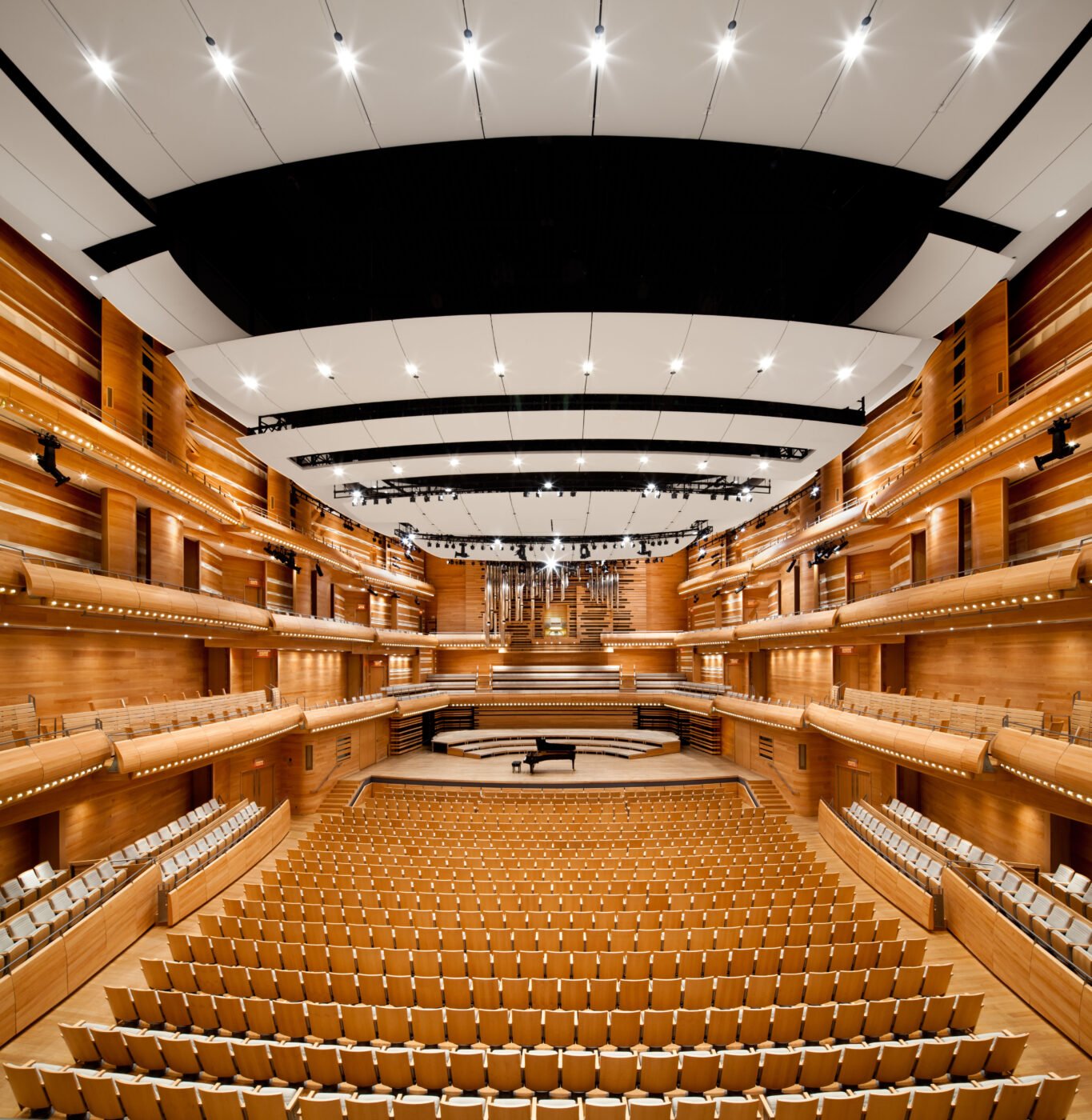 Une salle de concert en bois avec sièges, scène et plafond avec éclairage.