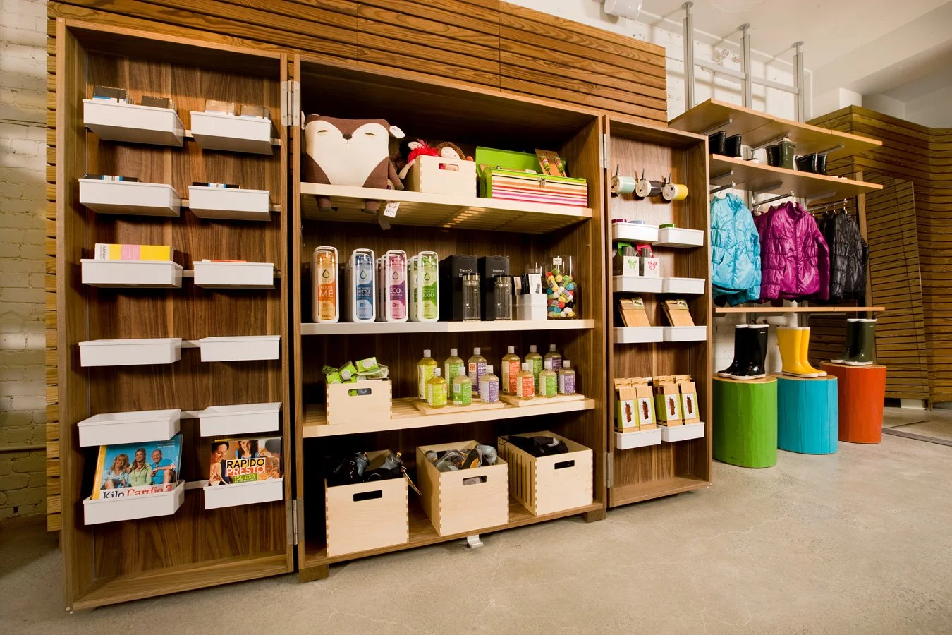 Étagères en bois avec divers produits, jouets, vêtements, bottes et chaussures dans un magasin.