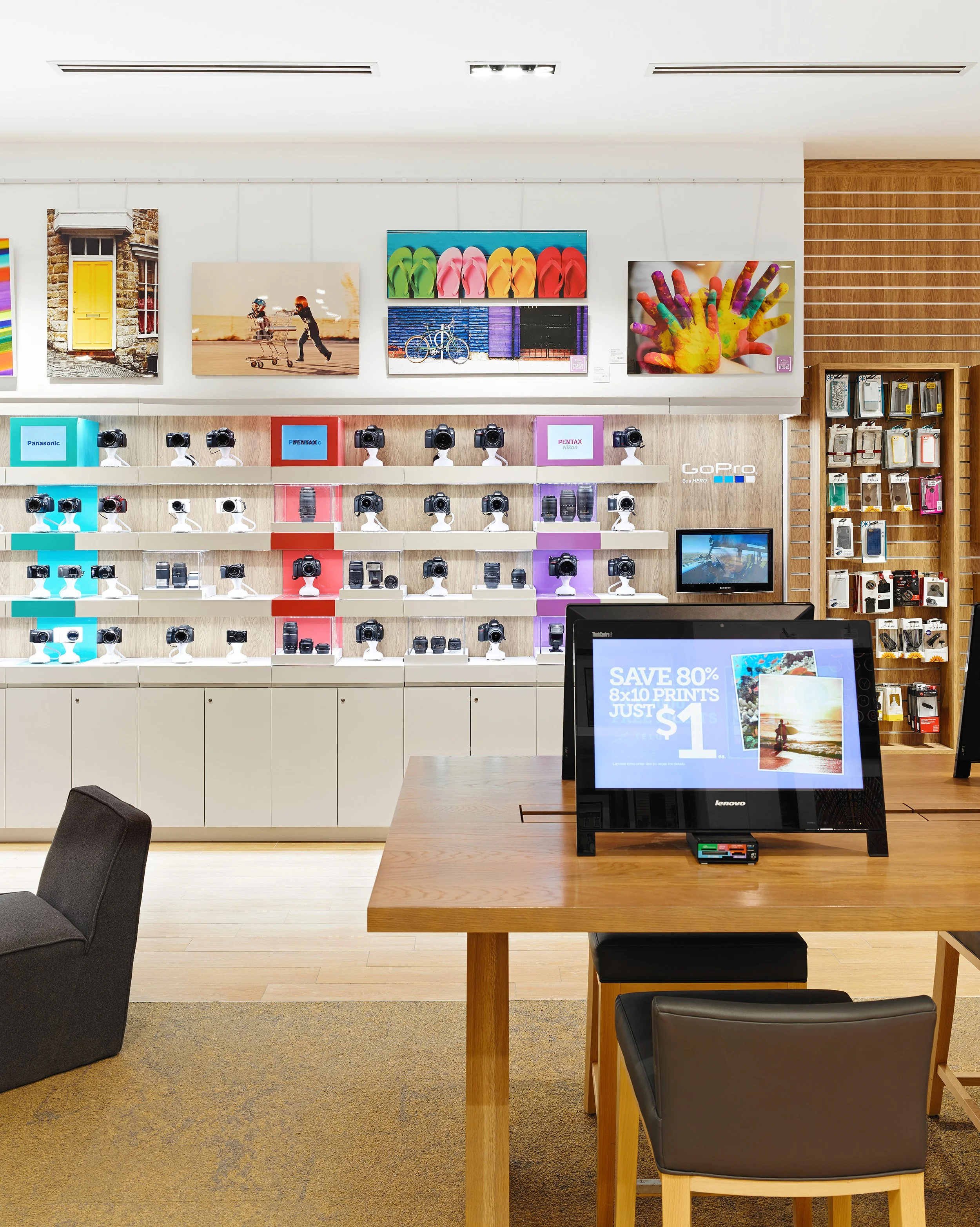 Magasin d'impression photo avec caméras, appareils photo et imprimantes, affichages numériques, et œuvres d'art accrochées aux murs.