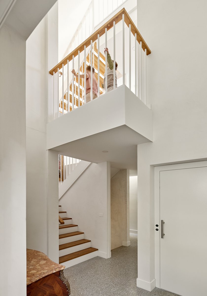 Two children walking on a staircase inside a modern home, viewed from below near the entrance.