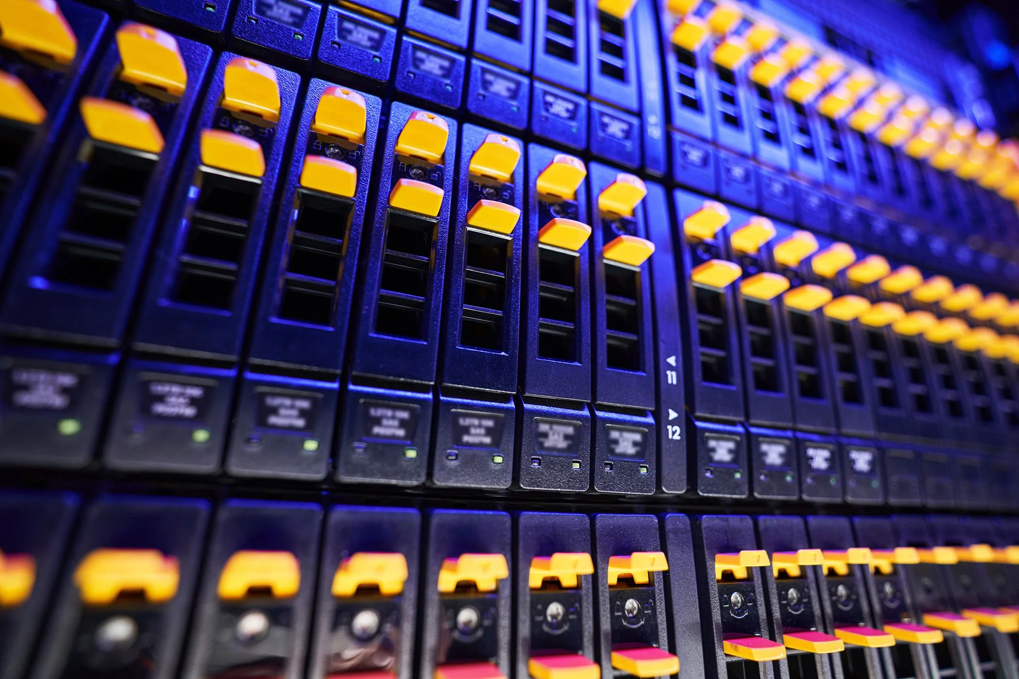Close-up of a professional audio mixing console with numerous sliders and buttons illuminated by blue and yellow lighting.