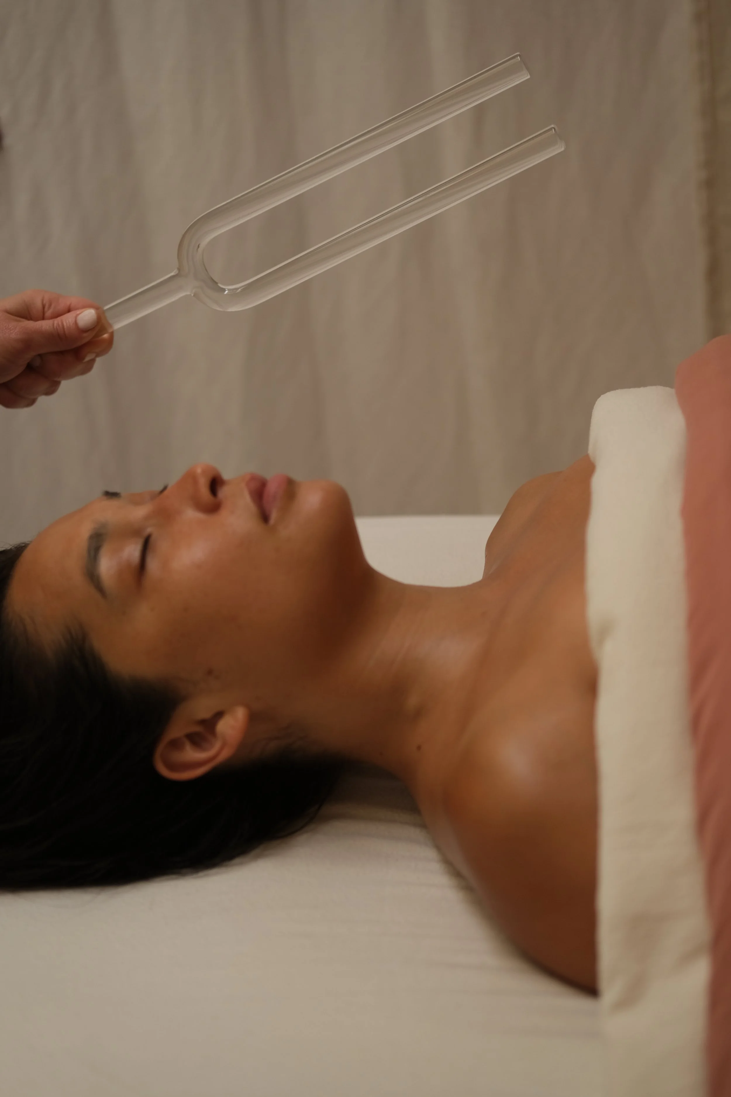 A woman lying on a white surface with her eyes closed, holding a glass water pipe (bong) above her face.