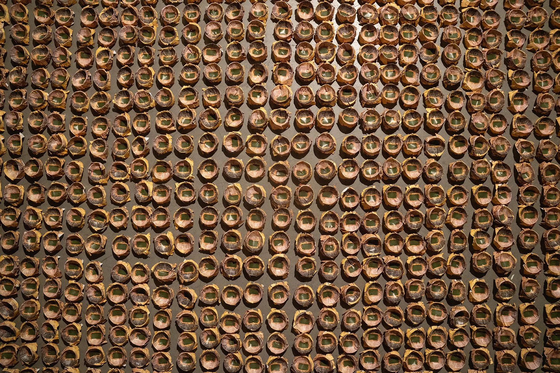 Close-up view of numerous brown wine corks arranged in a grid pattern, with some showing greenish stamps or marks on their ends.