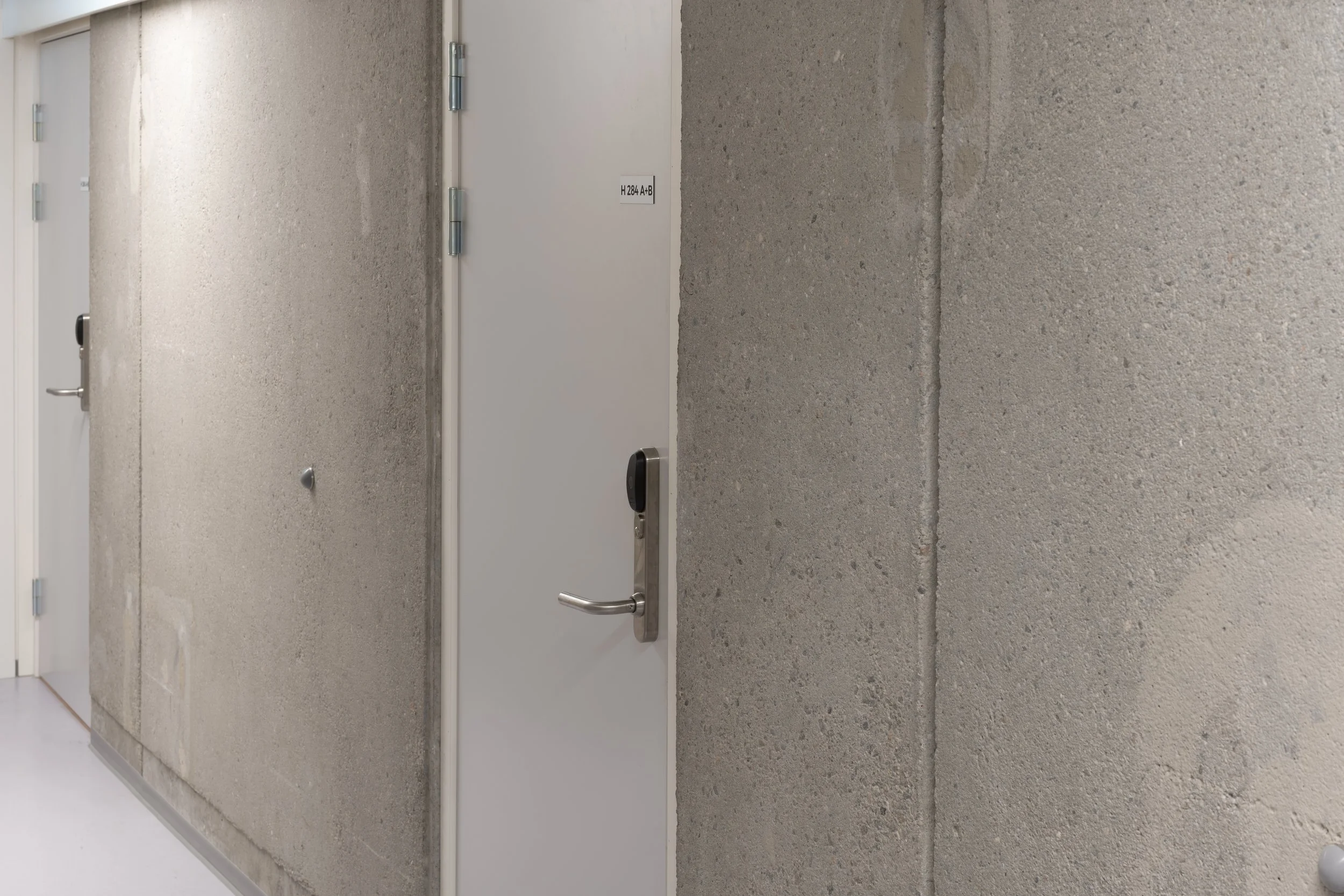 Gray wall with a door equipped with a silver door handle and a black electronic lock, and a small label that reads 'H 284 A B'.