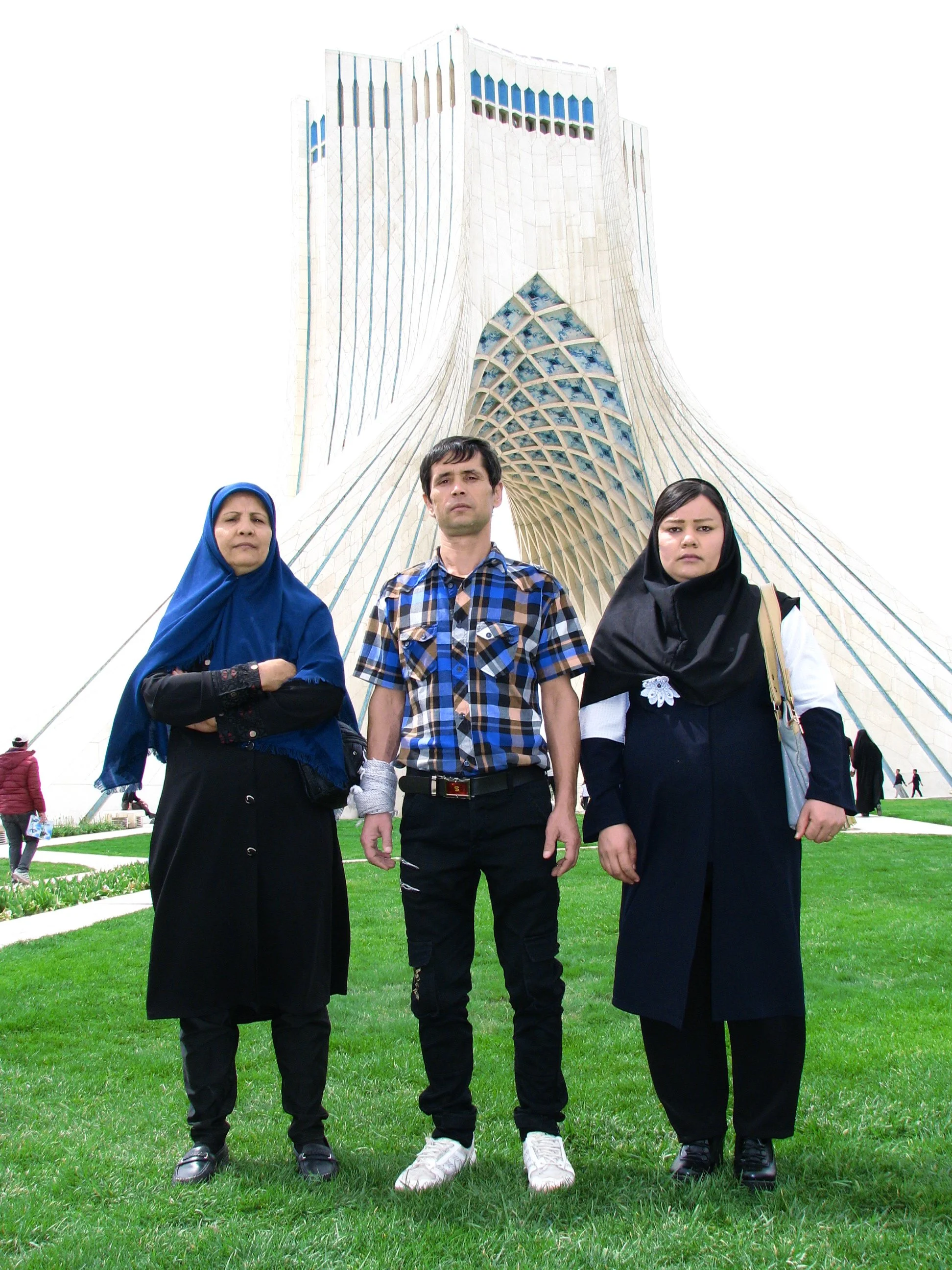 Three people standing on grass in front of a modern, tall building with an arch-shaped design.