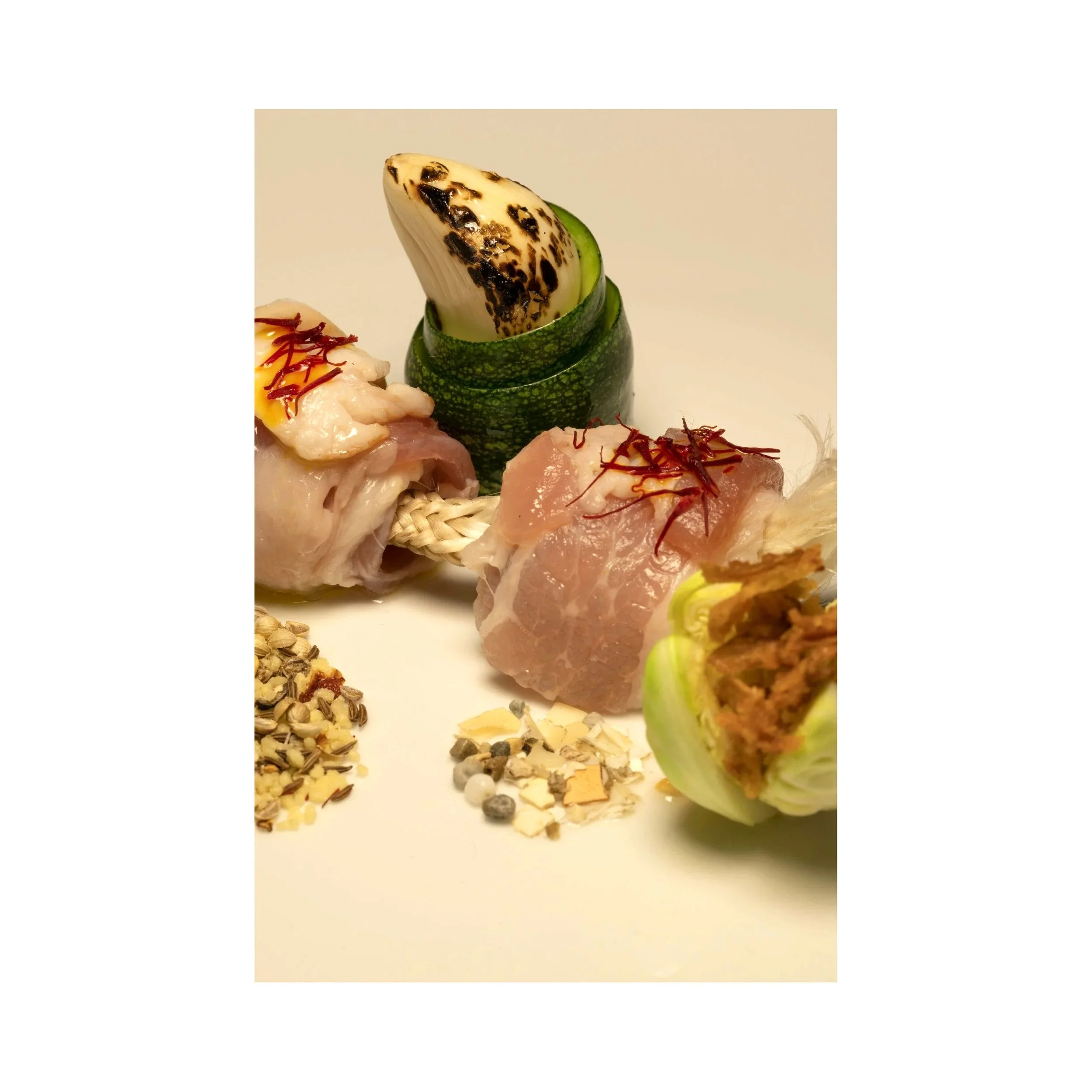 Raw chicken wrapped around a rope, garnished with chili threads, served with roasted zucchini, grilled onion, and mixed spices.