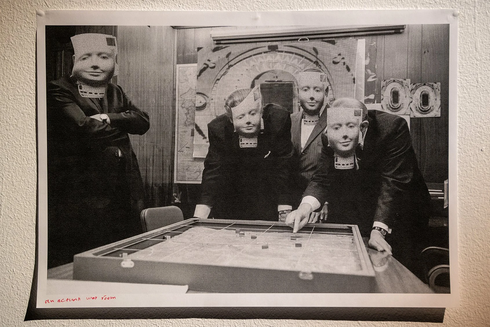 Black and white photo of five men in suits and old-fashioned paper masks, gathered around a table with a map, in a wood-paneled room decorated with art and large numbers, with handwritten text 'an actual war room' in the bottom corner.