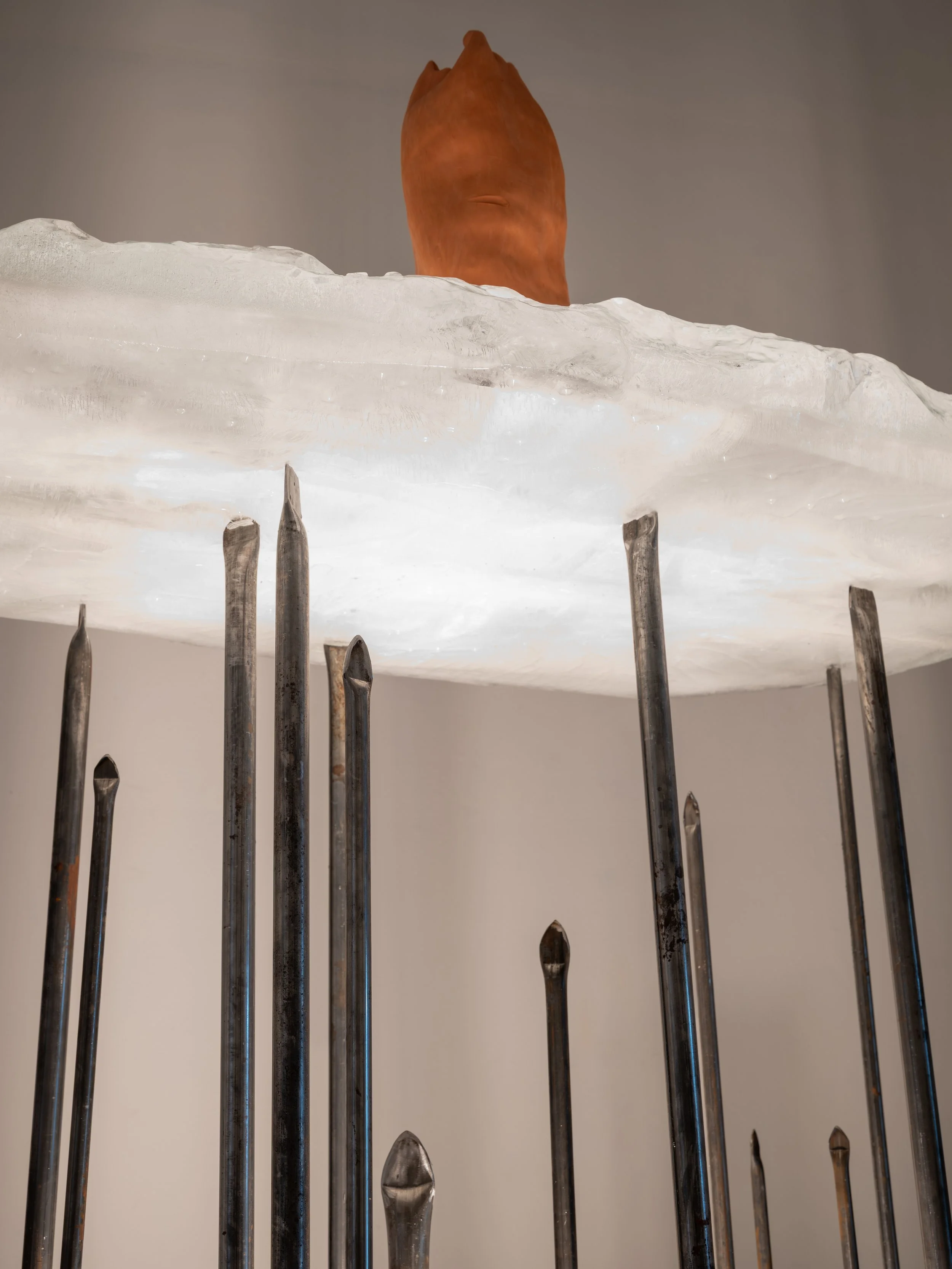 An art sculpture featuring a large white cloud with metal nails or stakes protruding from their bases, and an orange object on top that resembles a nose.