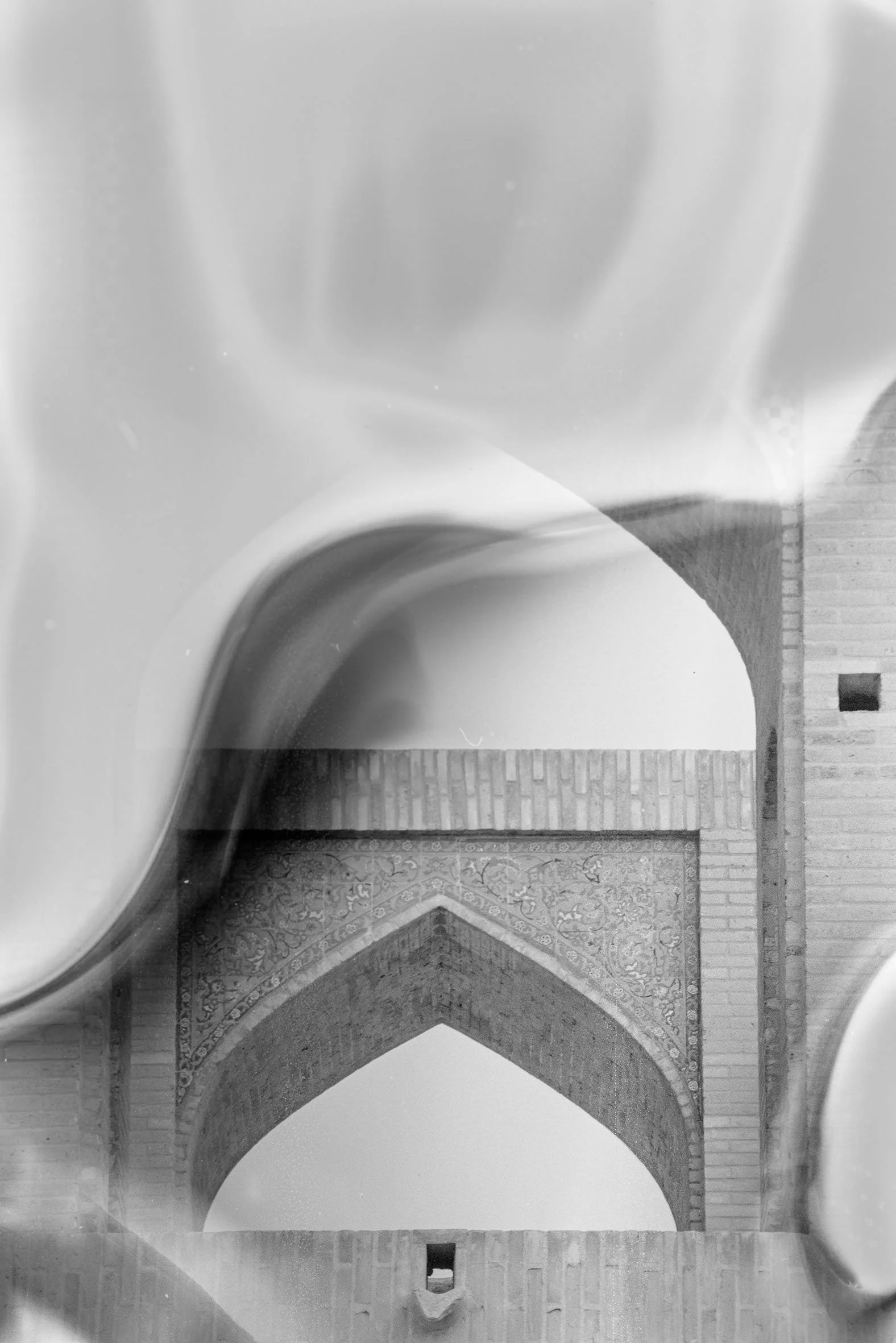 A black and white photo of an architectural structure with arched brick and tile design, viewed through reflective glass or surface.