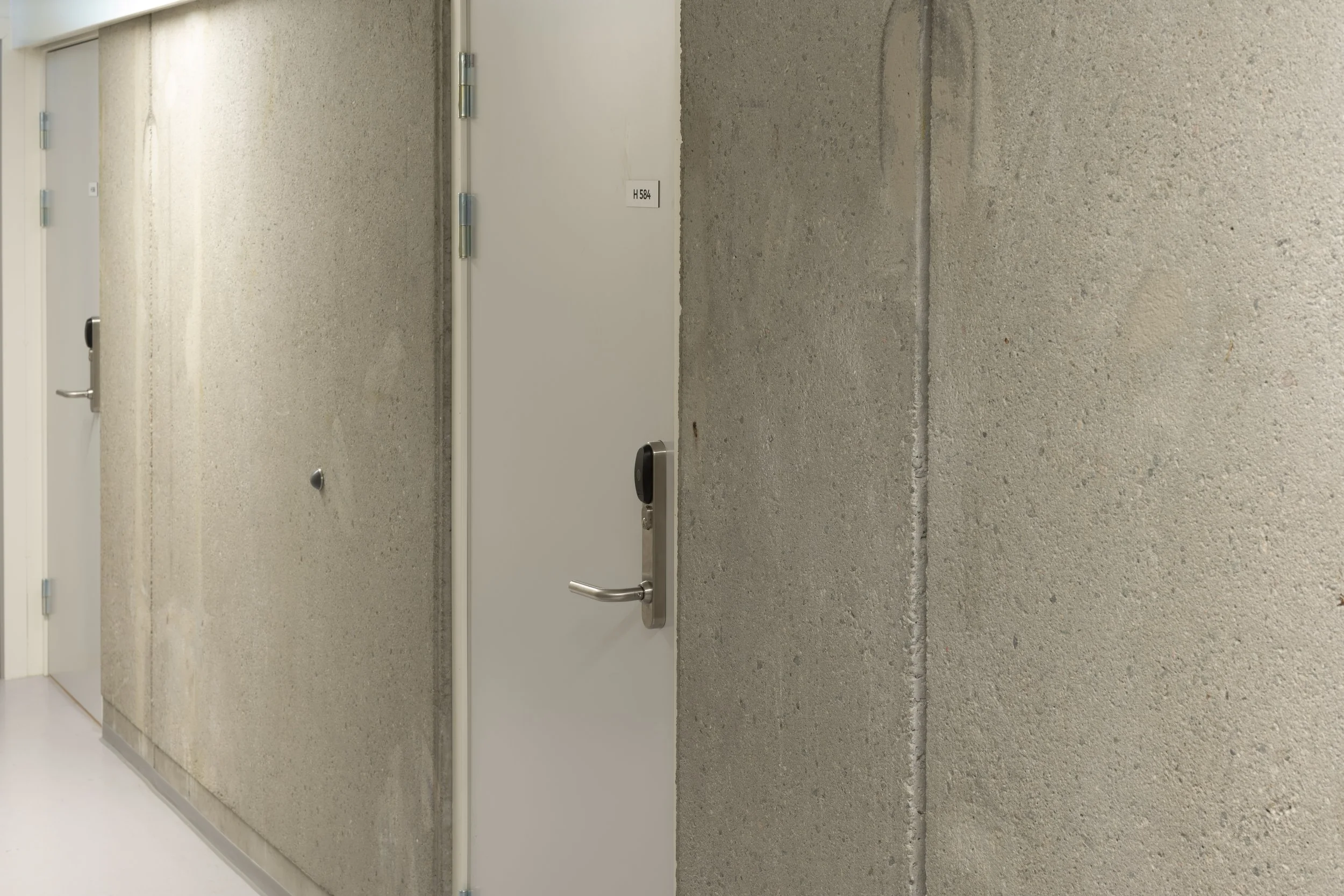 Interior of a building hallway with a concrete wall and a closed white door with a silver handle.