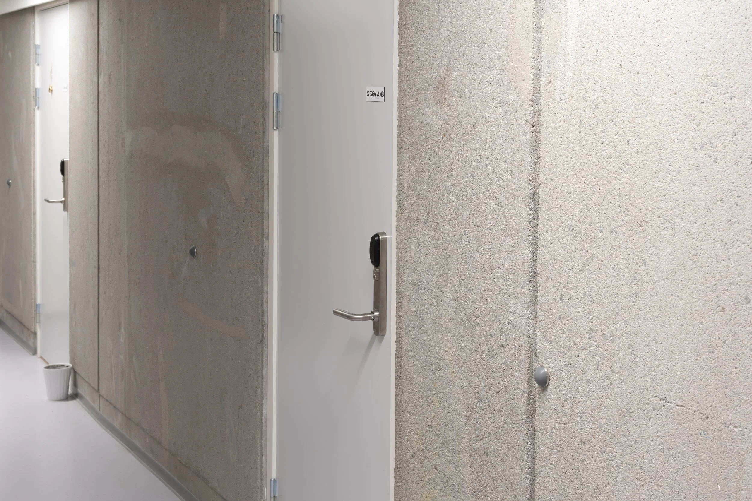 A plain white door with a handle and a digital lock, set in a gray concrete wall in a modern hallway.