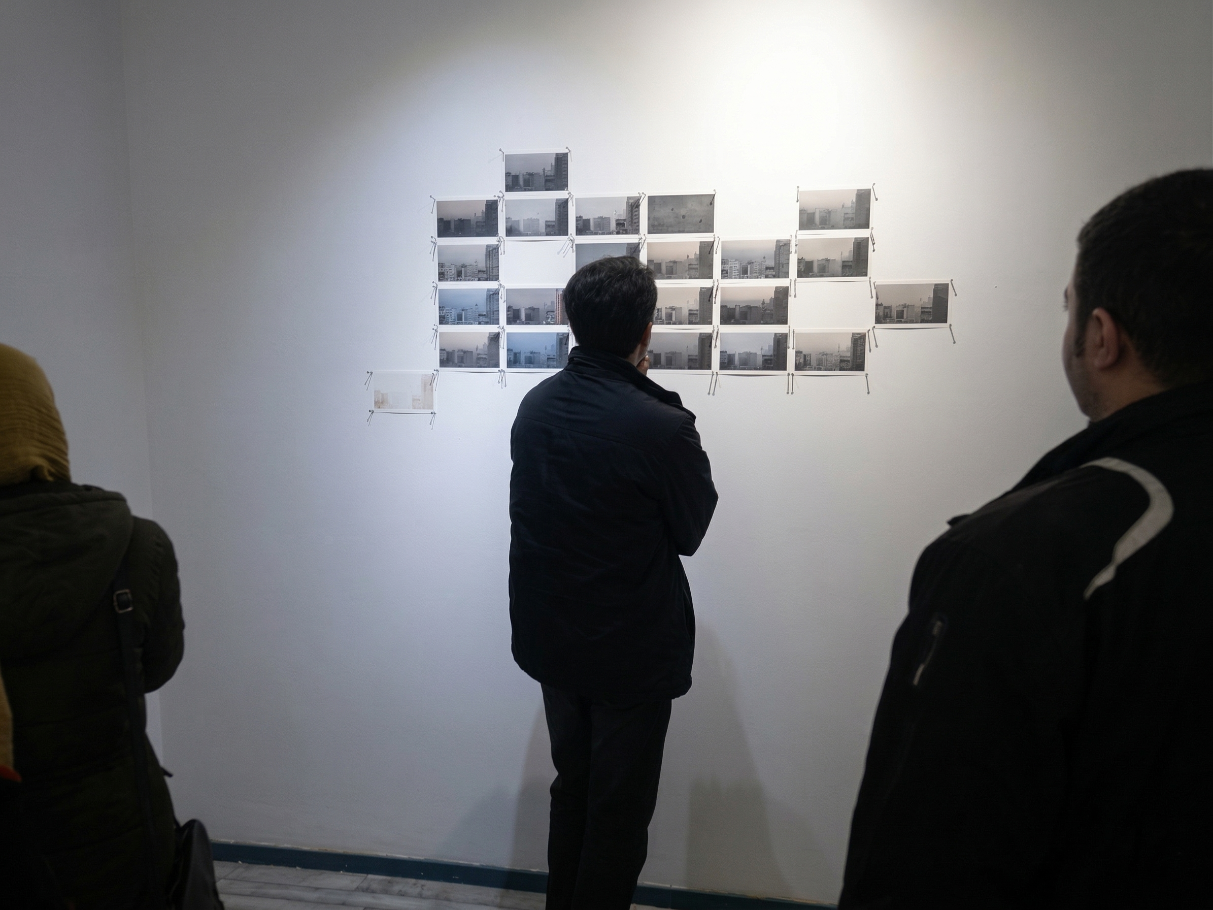 Three people viewing black-and-white photographs of cityscapes displayed on a wall in an art gallery.