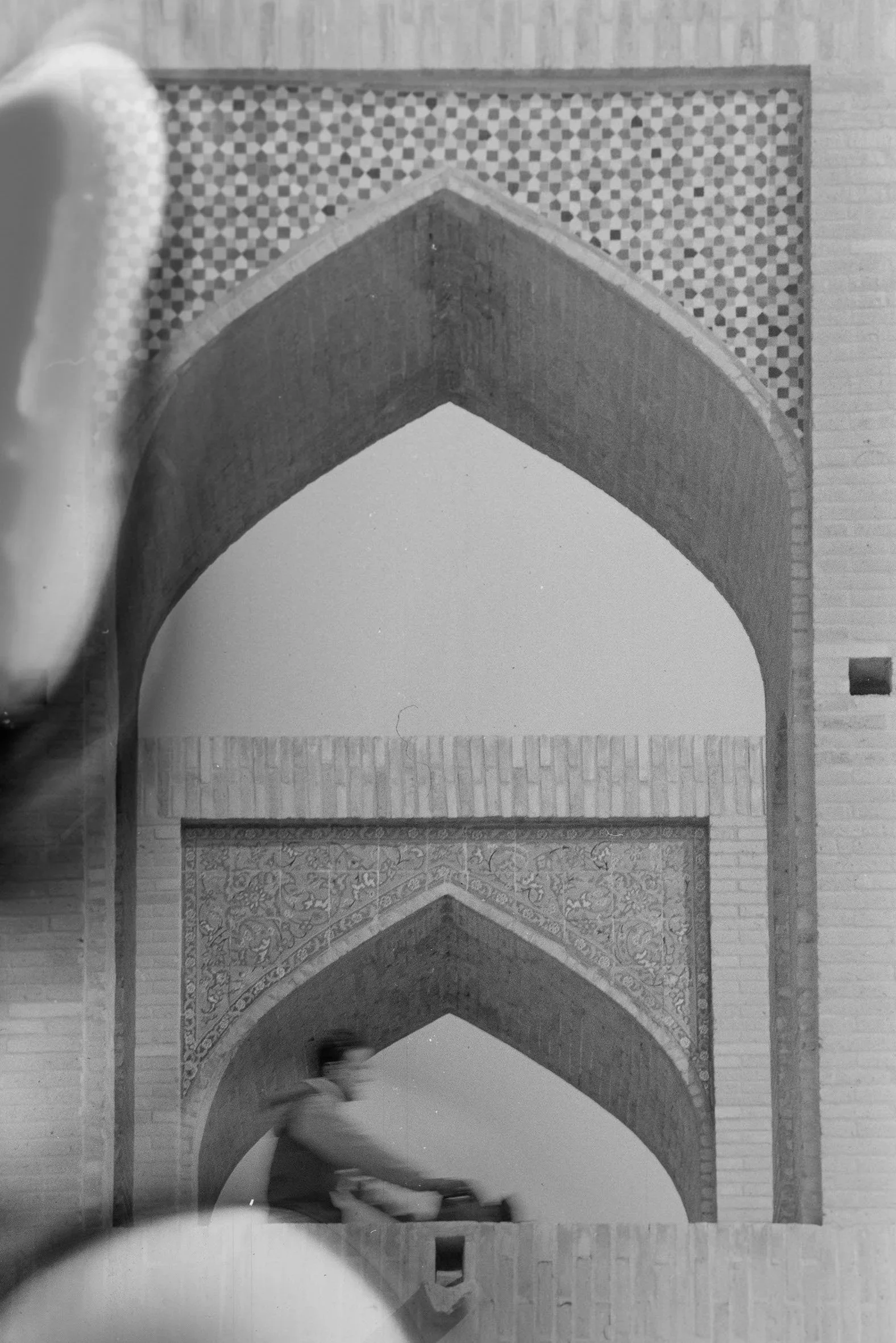 View of an interior architectural feature with three pointed arches and decorative brickwork, with a blurred person walking in the foreground.