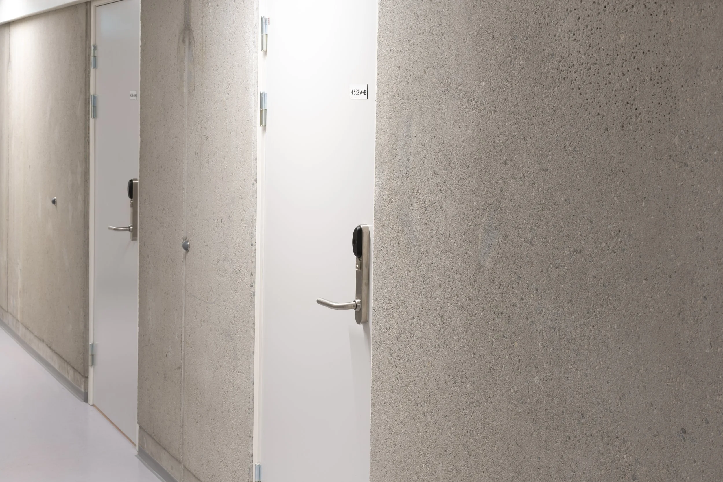 A hallway with multiple closed white doors, each with a silver handle and electronic lock, and beige textured walls.