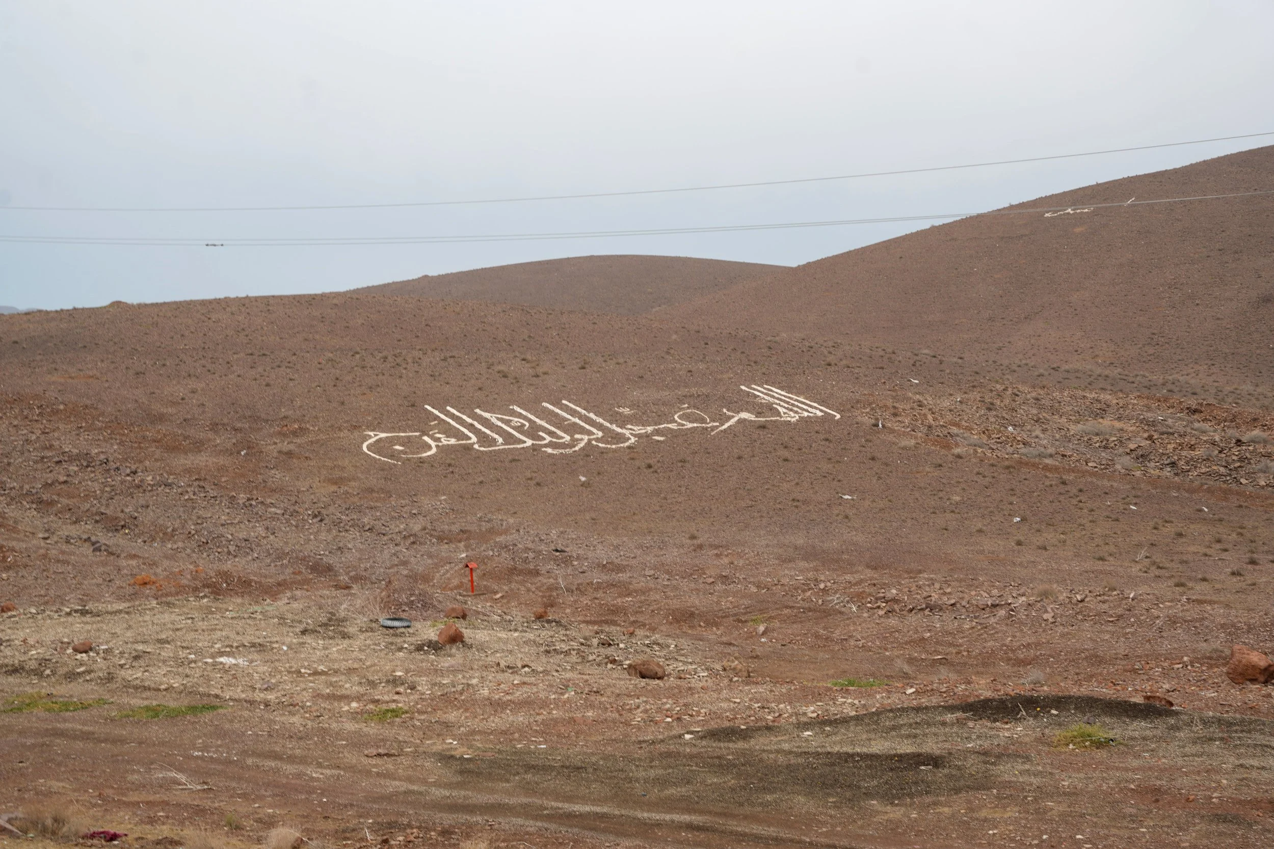 A desert landscape with a large white Arabic inscription on the hillside that says 'Allahu Akbar'.