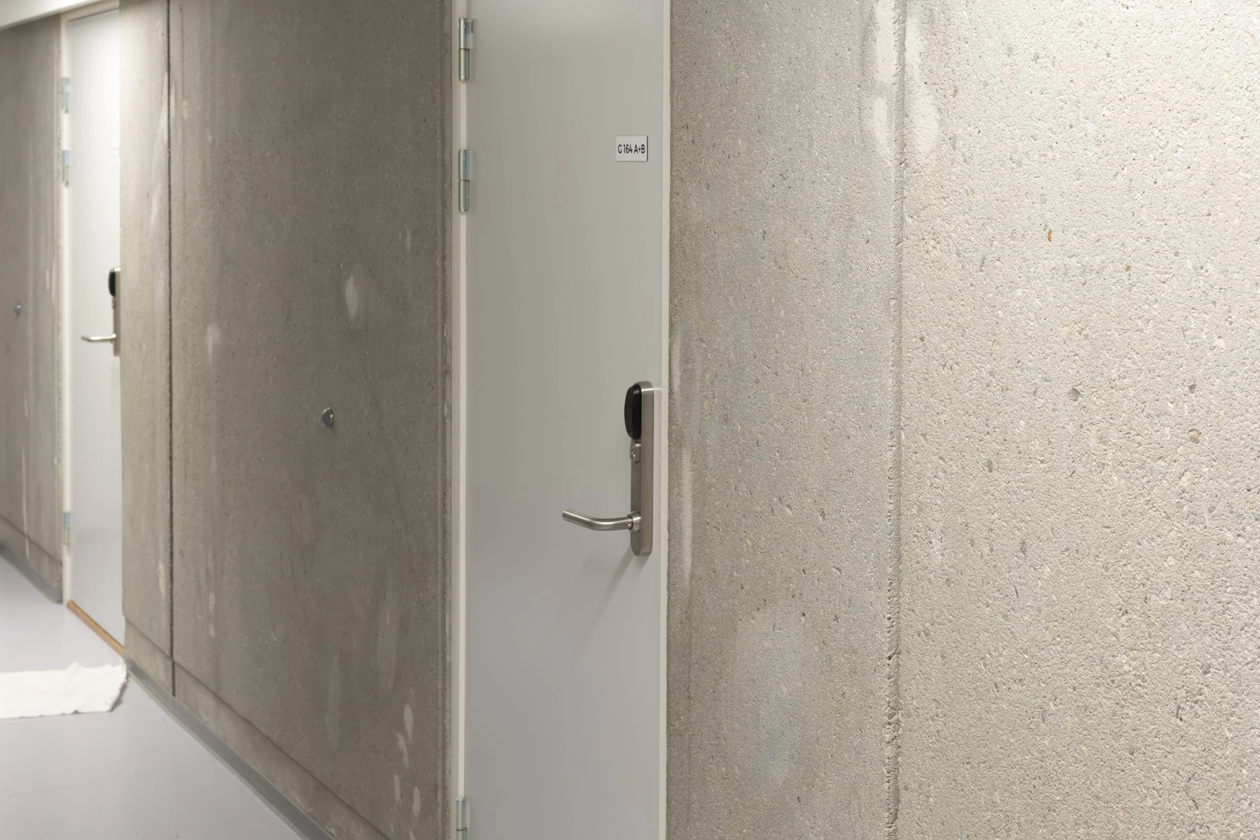 A corridor with a row of metal safe deposit boxes and a white door with a handle and electronic lock.