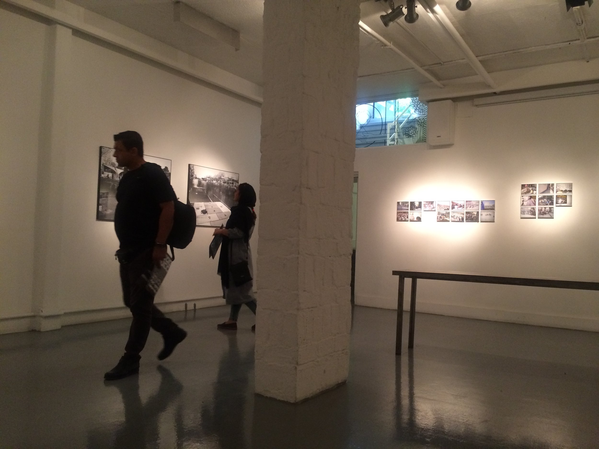 People viewing photographs in an art gallery with white walls, soft lighting, and a brick pillar in the center.