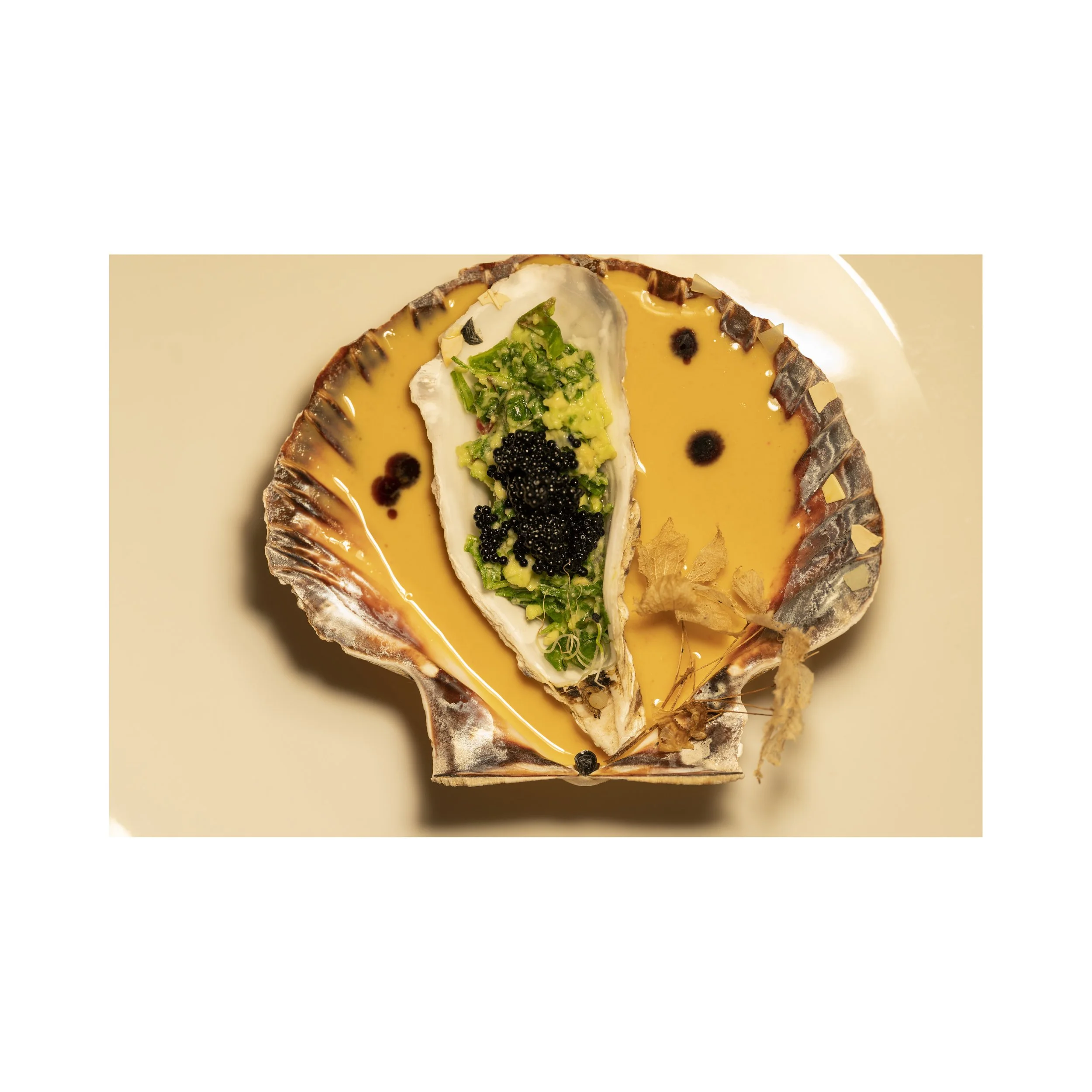 A shell with a creamy yellow filling topped with green herbs, black caviar, and small black beads.