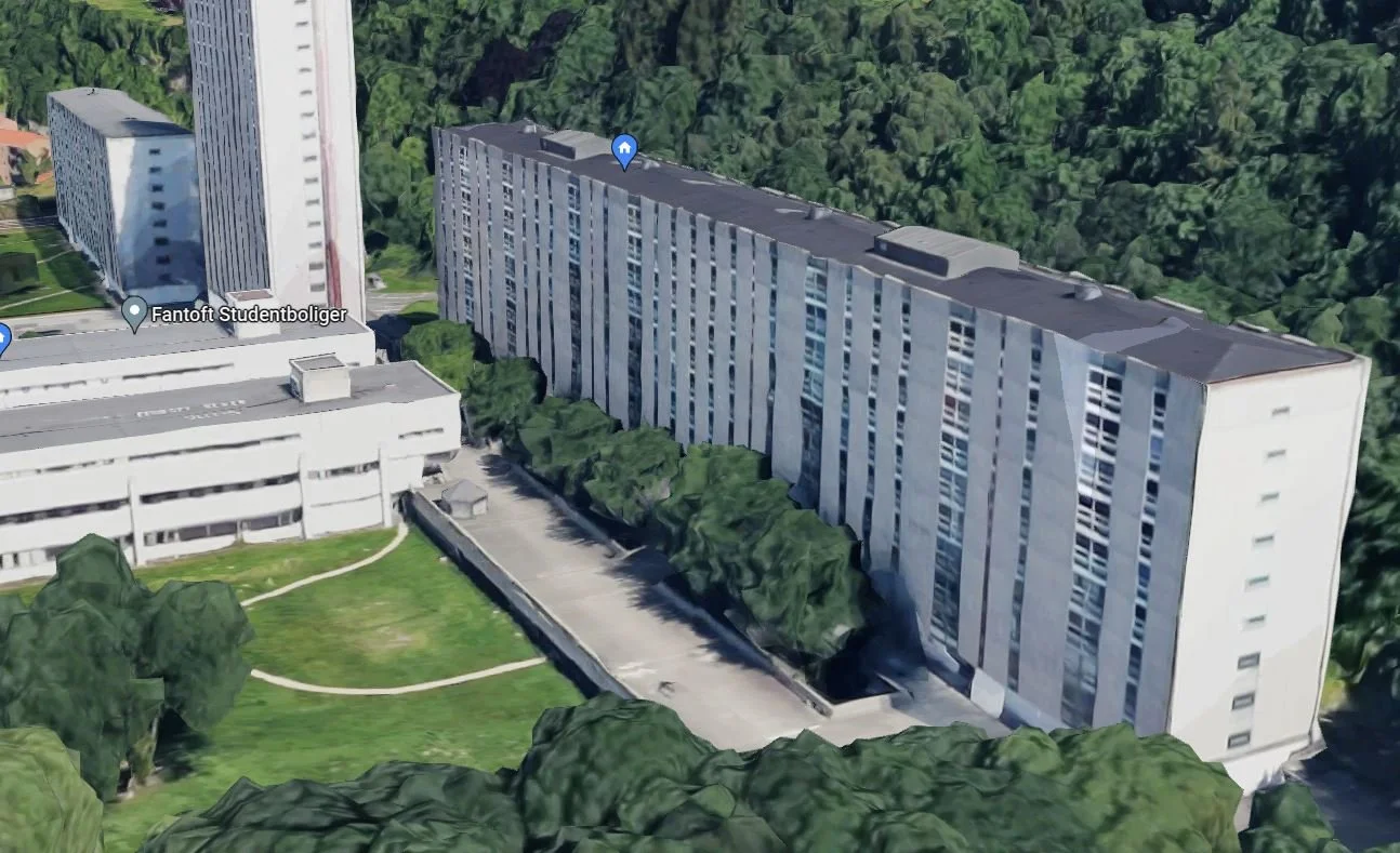 Aerial view of a multi-story residential building surrounded by trees and green lawn with walking paths.
