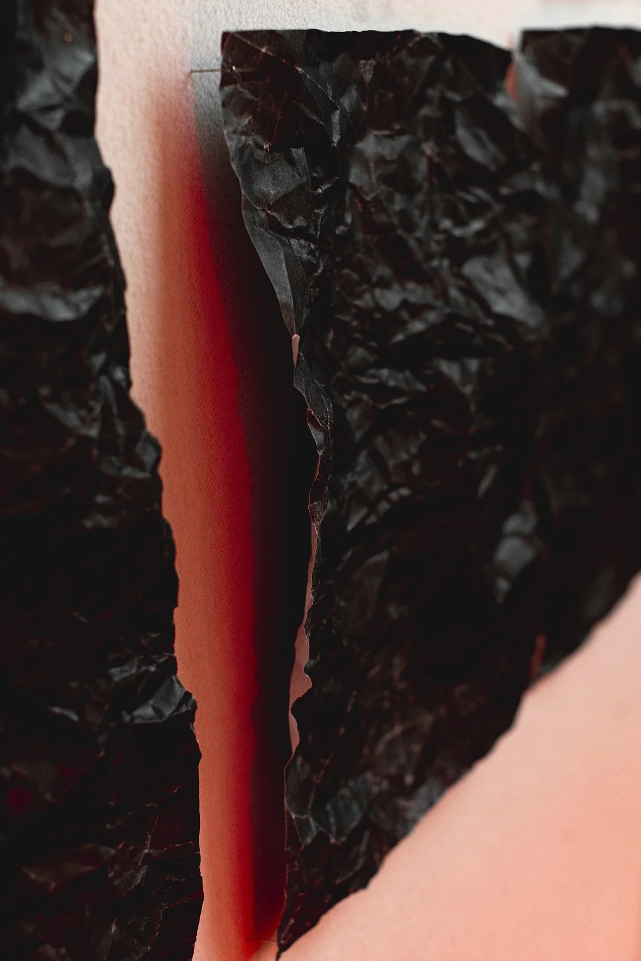 Close-up of torn black textured paper revealing red and pink layered paper underneath.