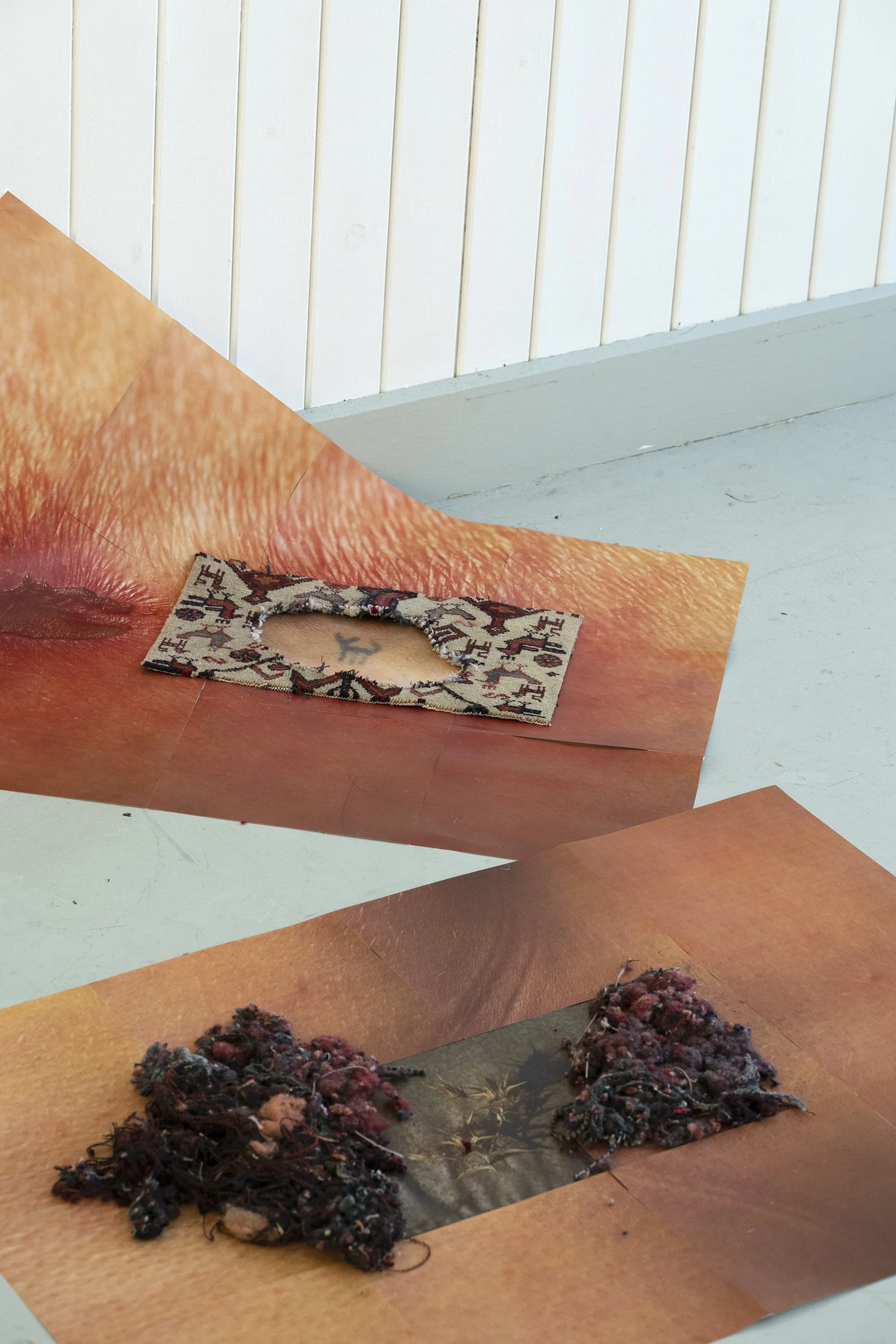 Mixed media art installation with torn magazine pages and textile pieces on orange-toned backgrounds.