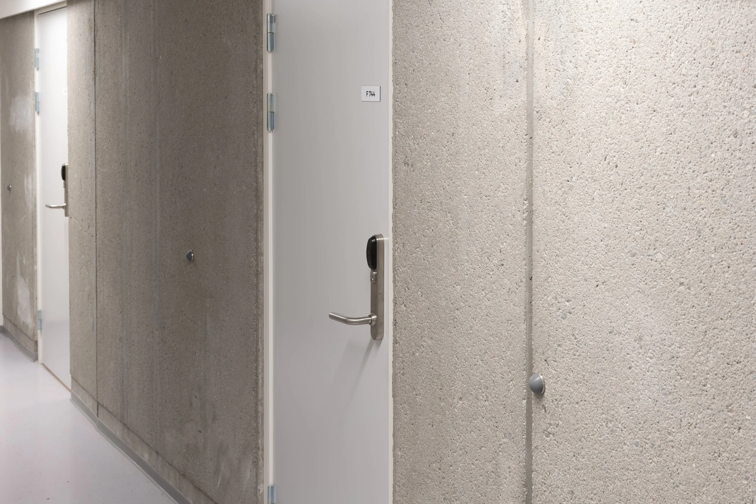 Hallway with gray textured walls, several doors, one with a keypad lock and a door label 'F744'