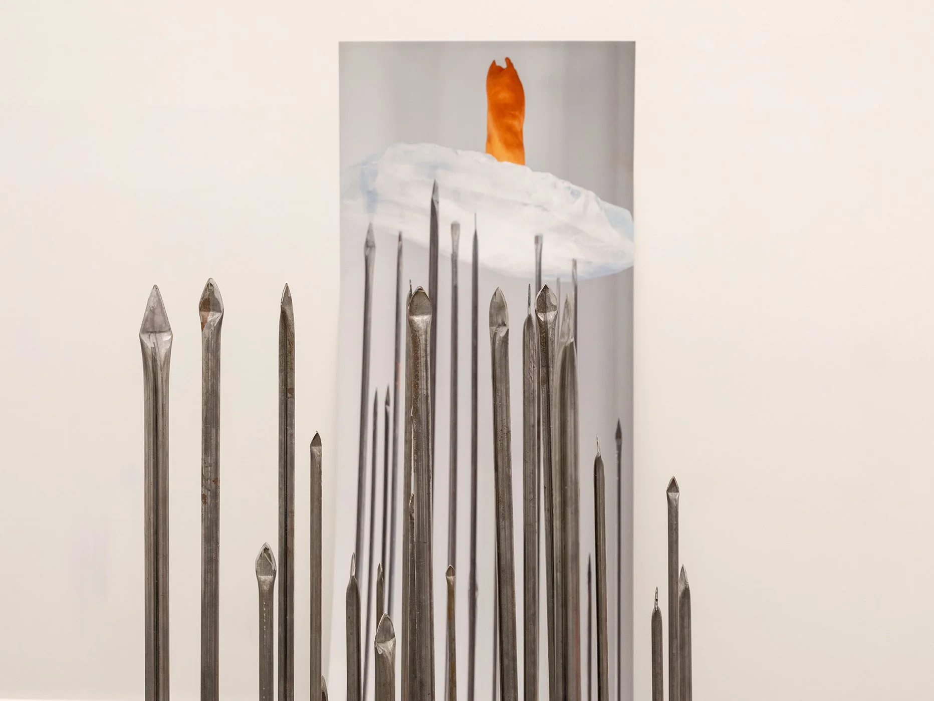 A group of steel pins arranged in a pattern with a painted backdrop of a mountain scene, featuring a cloud and a cat statue on top of the mountain.