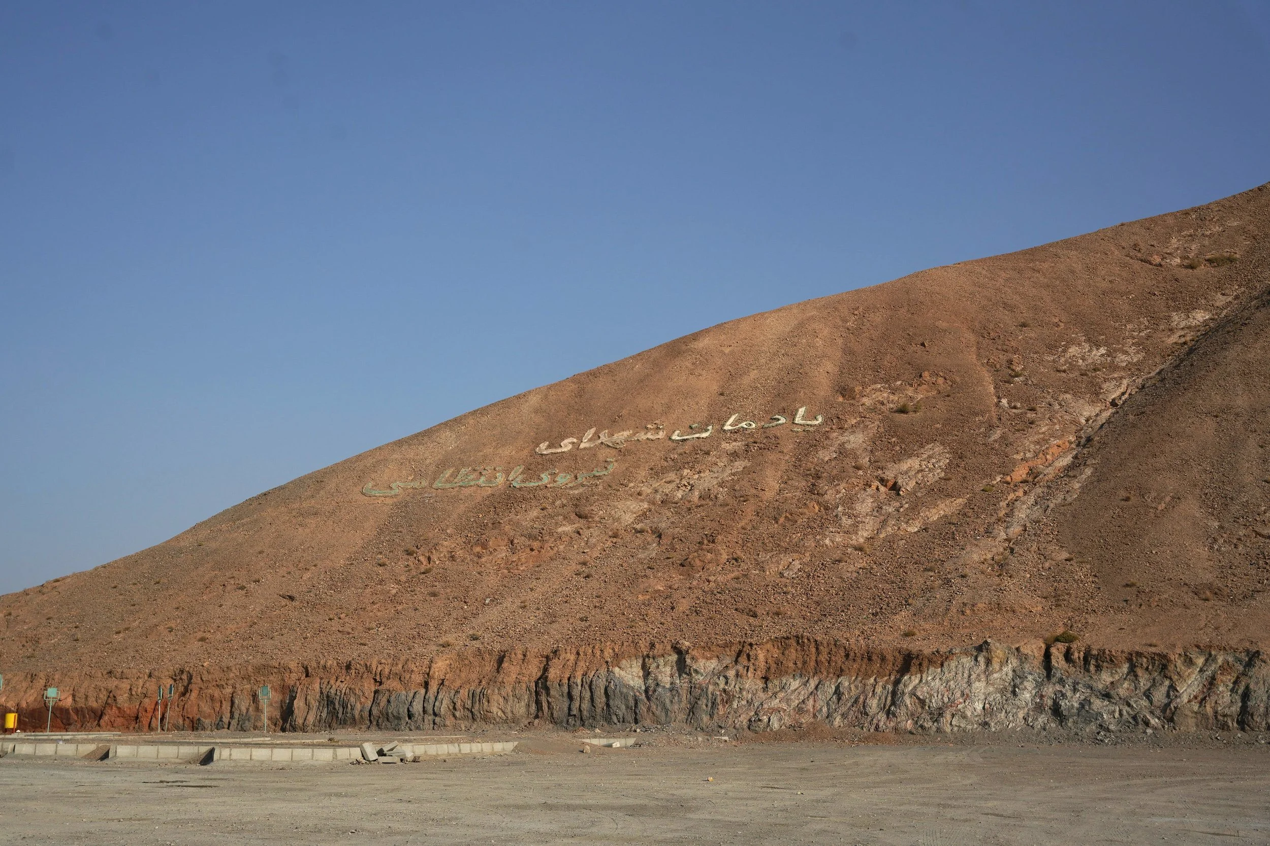 A hillside with Persian writing on it, under a clear blue sky.
