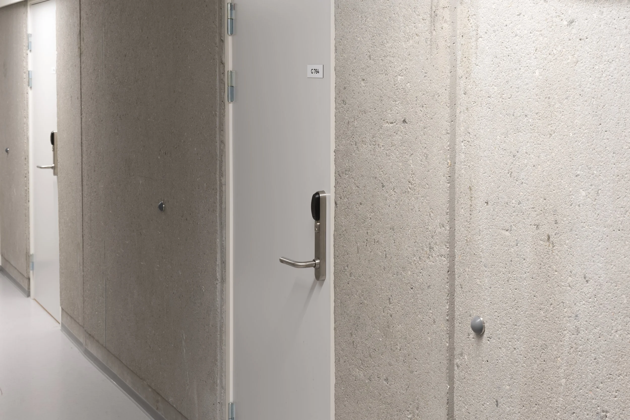 A hallway with beige textured walls, doors with metallic handles, and a door sign that reads 'C764'.