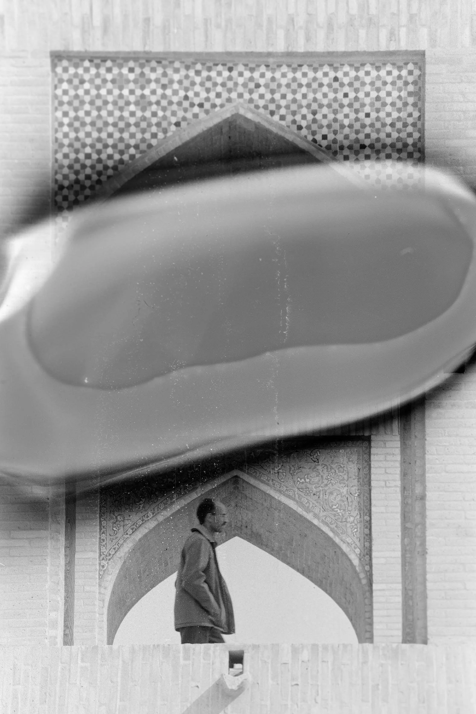 A man walking past a decorative archway in front of a building, with a large, blurred object in the foreground.