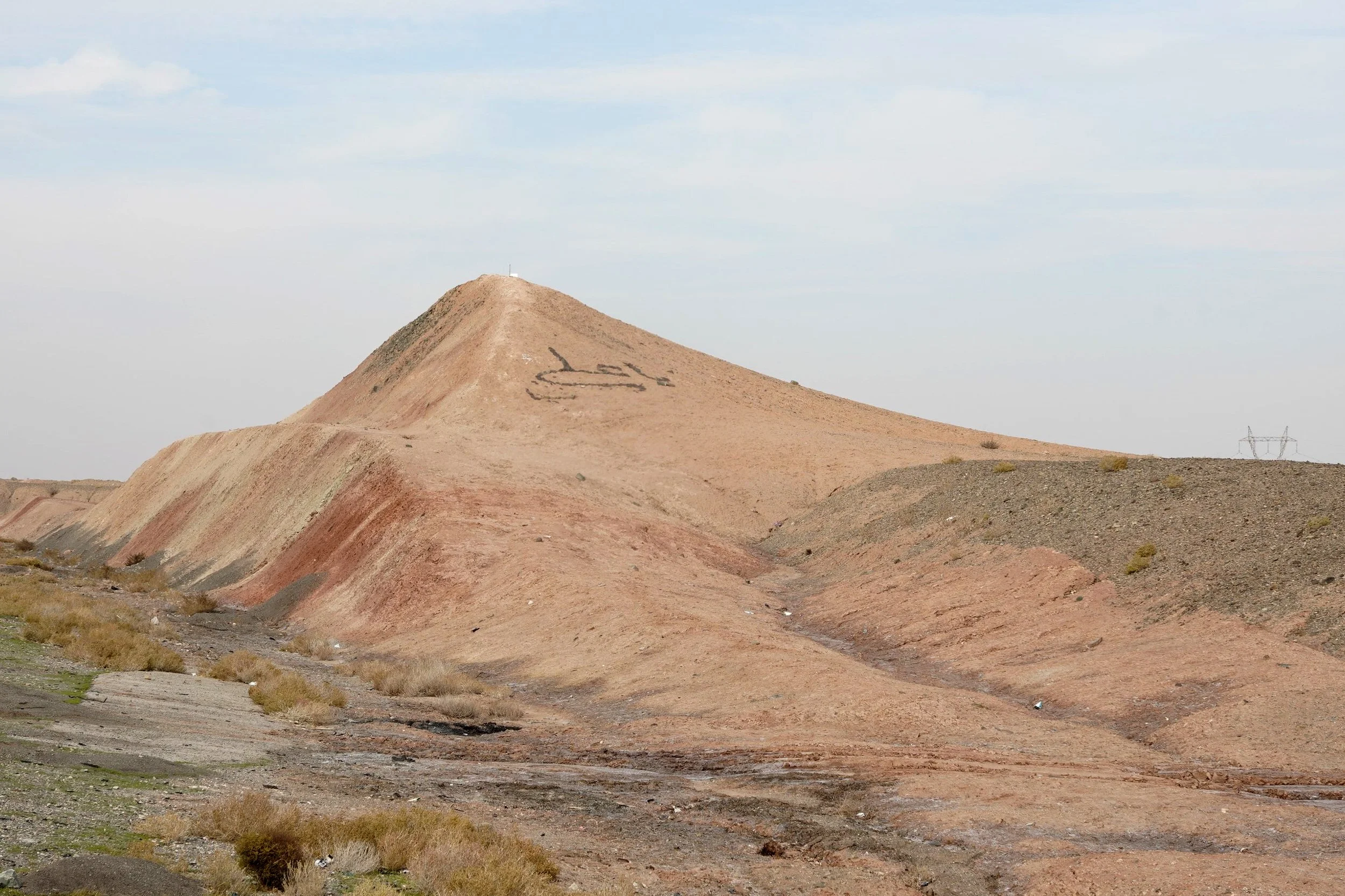 A barren, rocky hillside with a dirt path winding up to a small cross at the top, and the word 'LIES' written on the hill.