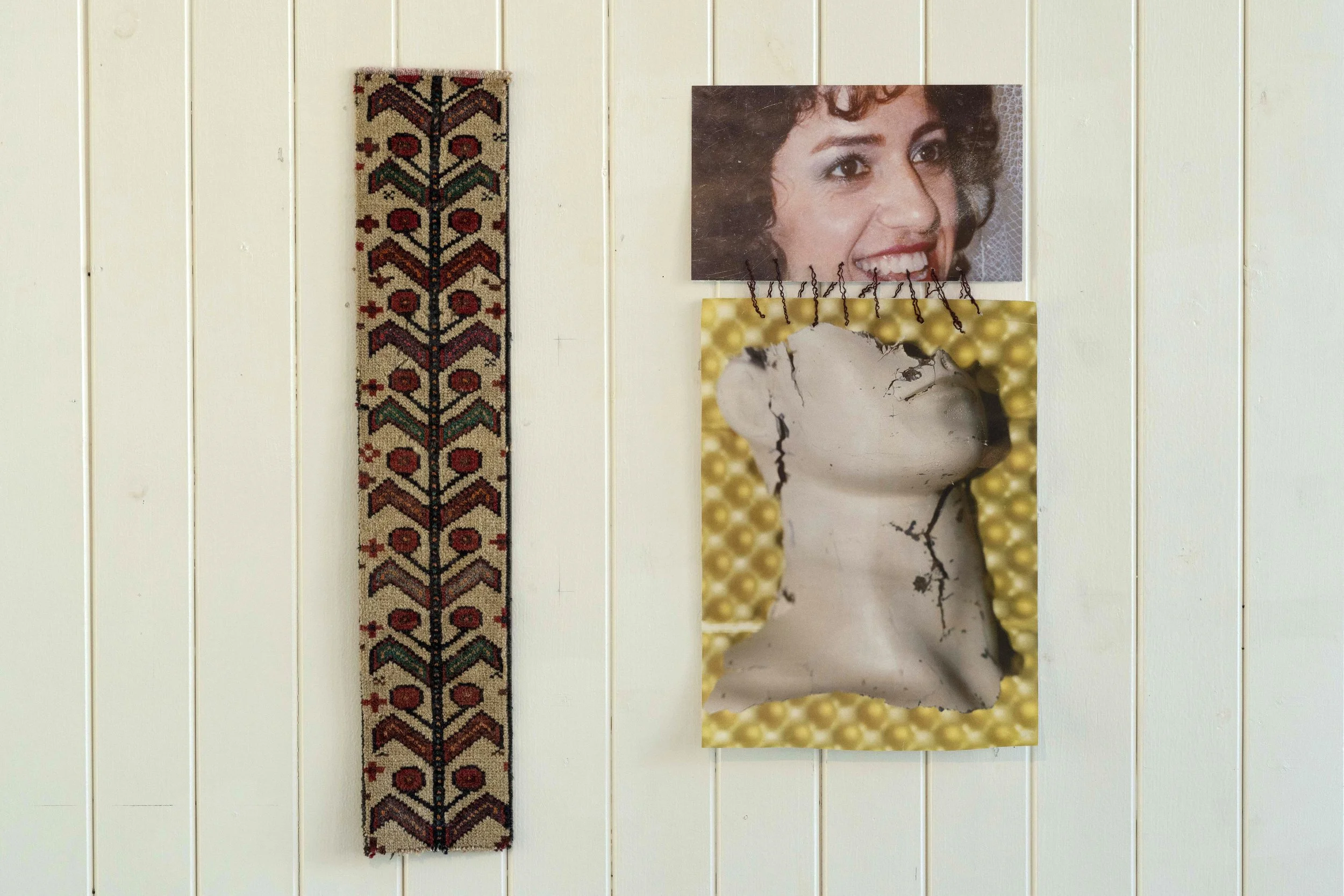 Decorative wall with a shaggy, vertically hanging textile and two mixed-media artworks, one of a woman's smiling face and a cracked, abstract sculpture face with a yellow background.