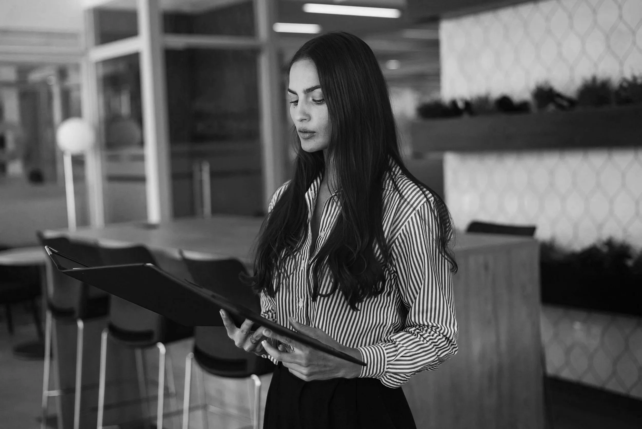 Professional woman reviewing documents near a bookshelf — black and white editorial photo, Elevated Accounting