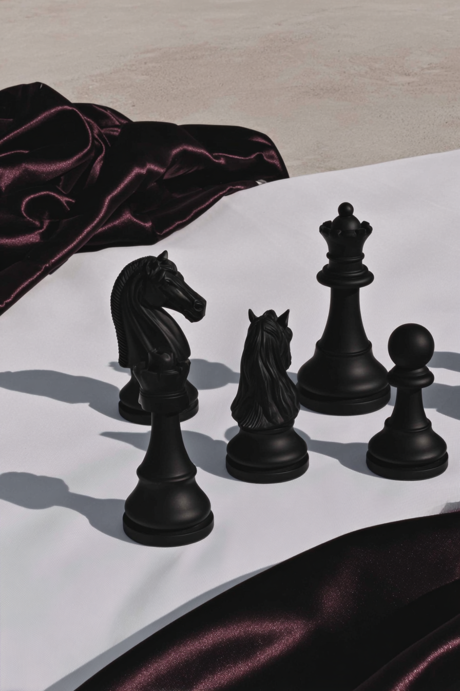 Black chess pieces arranged on a white surface with dark silk fabric — editorial brand image representing strategic financial planning, Elevated Accounting