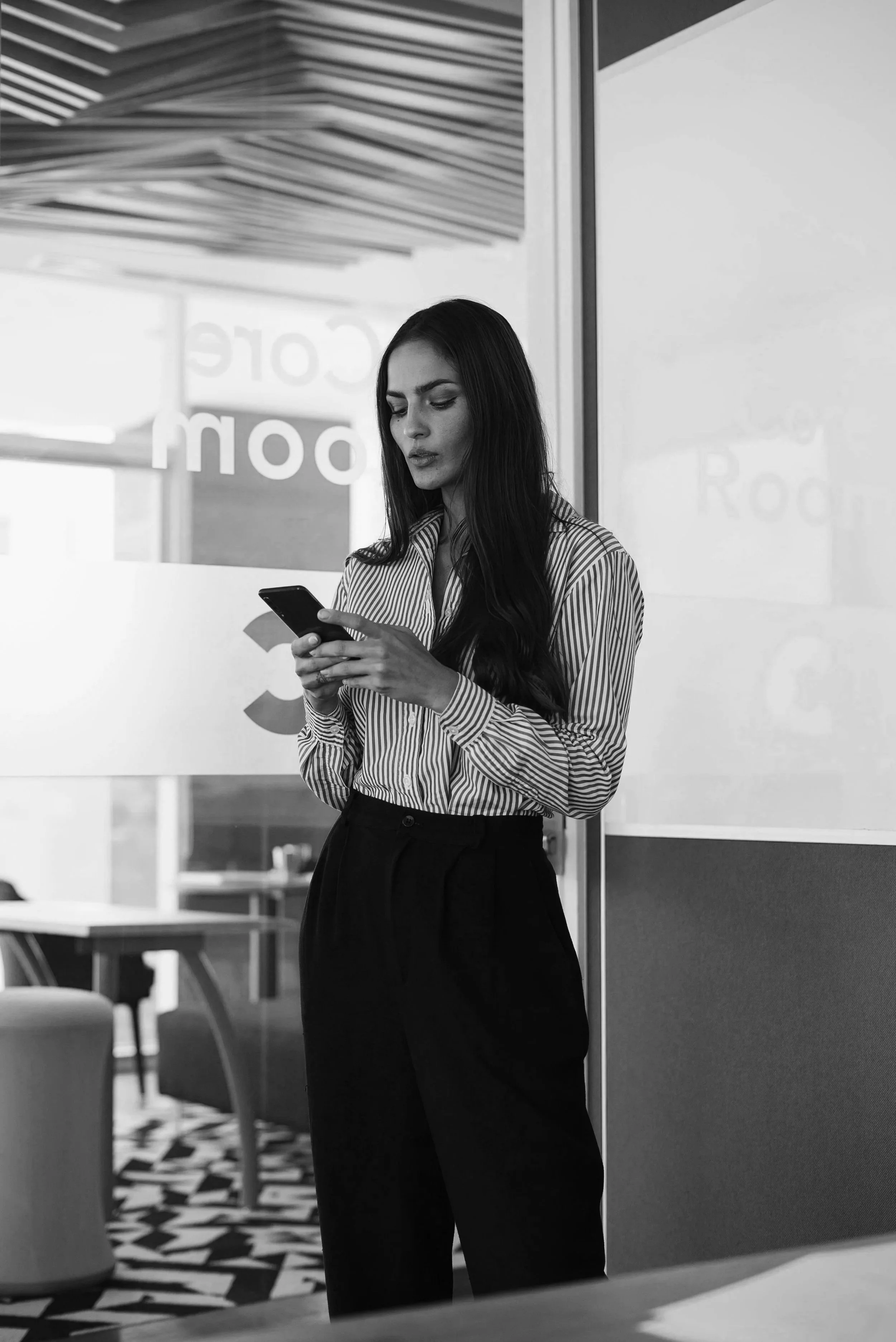 Professional woman in a striped blazer looking down at her phone — black and white editorial photo, Elevated Accounting