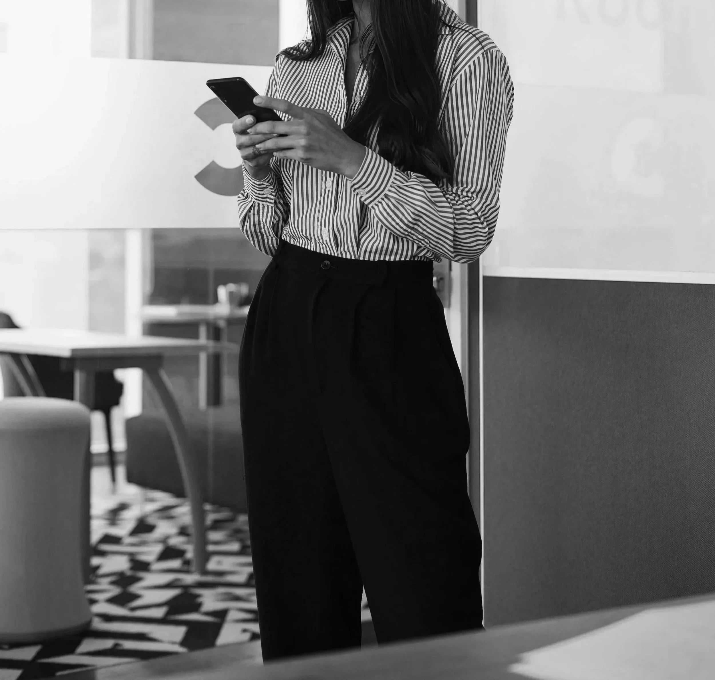 Professional woman in a striped blouse and wide-leg black trousers holding a phone — black and white editorial brand image, Elevated Accounting CFO on Call