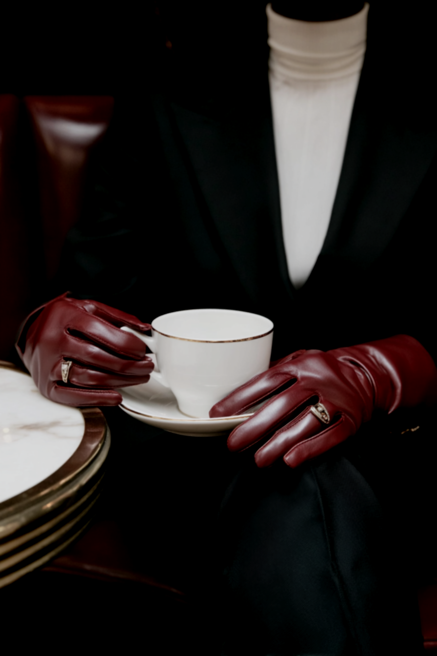 Gloved hands in dark burgundy leather holding a fine china teacup and saucer — editorial brand image for Elevated Accounting