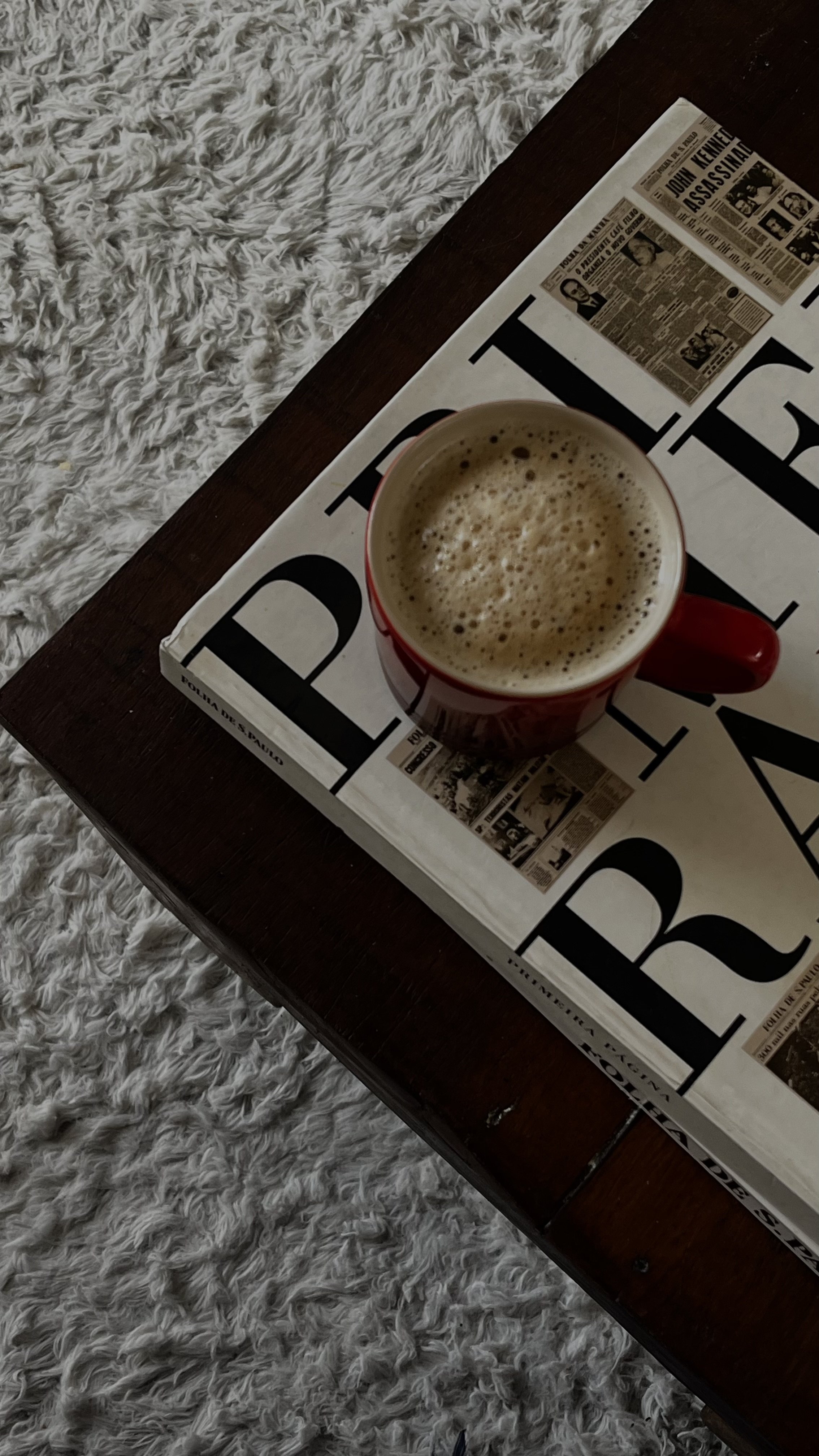 Red coffee mug resting on an open newspaper, shot from above on a white textured surface — editorial brand image representing intentional quarterly financial review, Elevated Accounting