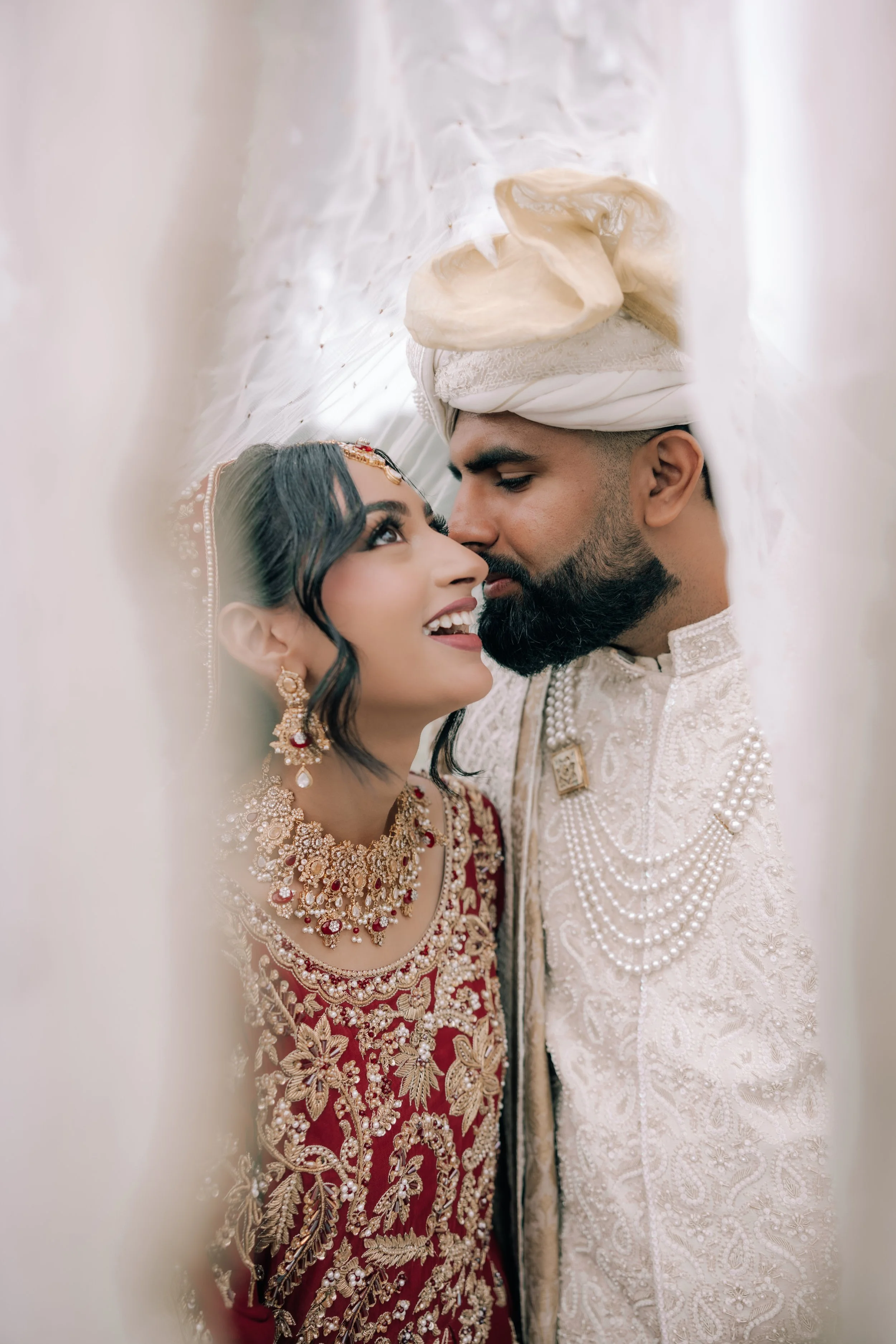 A close-up of an Indian bride and groom during a wedding ceremony, dressed in traditional wedding attire with jewelry, standing very close to each other with foreheads touching.